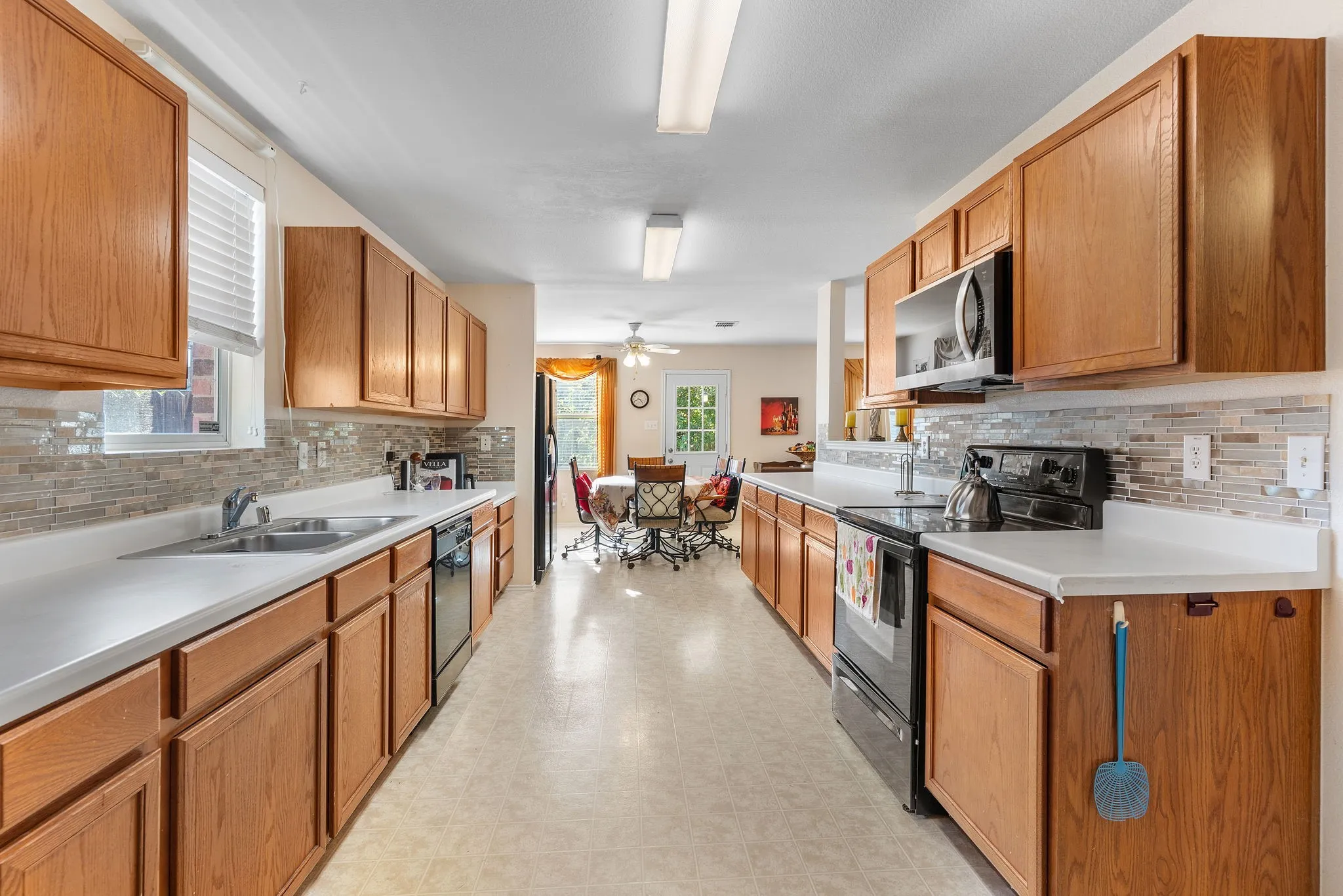 Galley kitchen featuring light wood-finish cabinetry, a subway tile backsplash, and white countertops