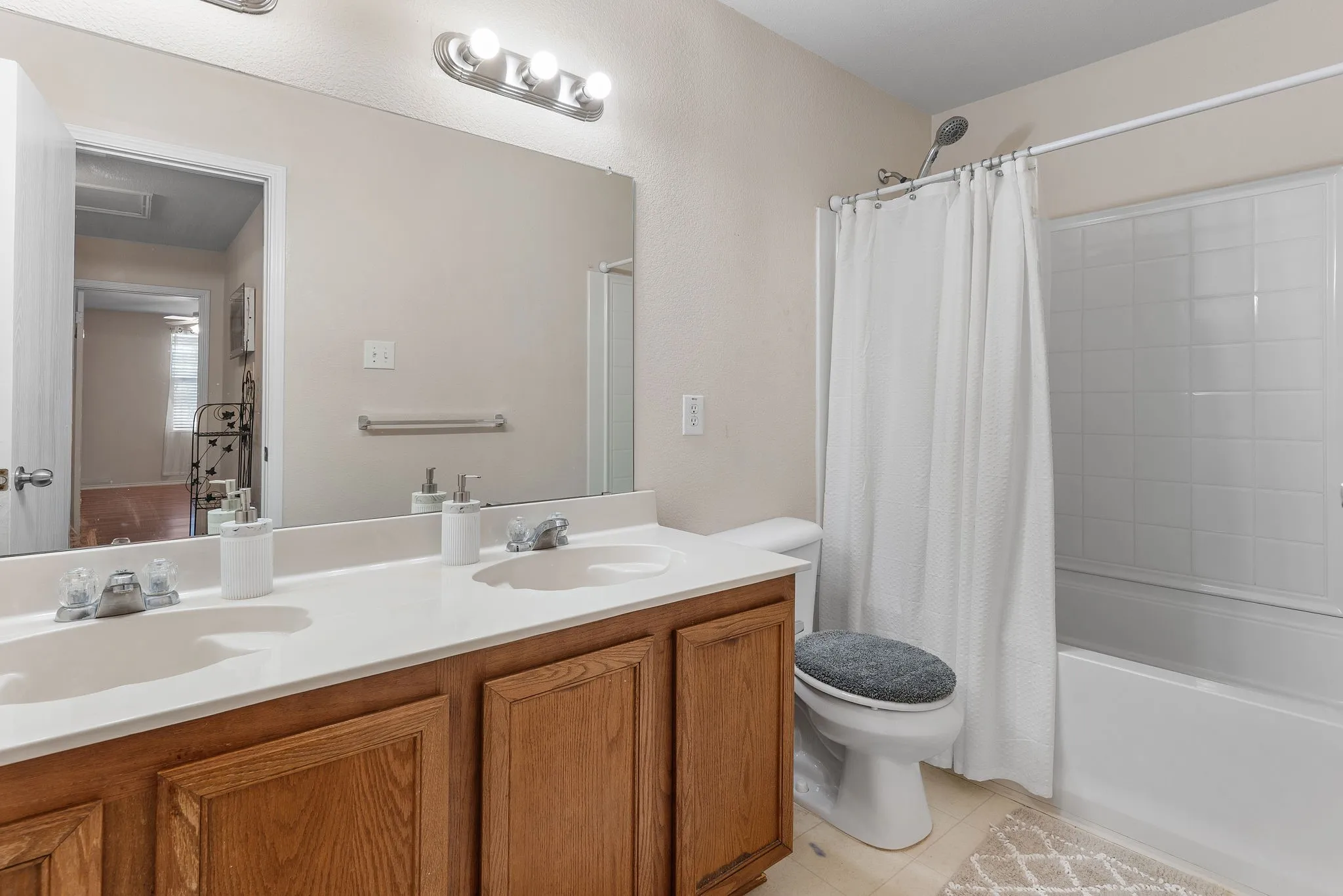 Dual vanity with integrated sinks, wood-finish cabinetry, full-width mirror, and a full-size bathtub with tiled surround
