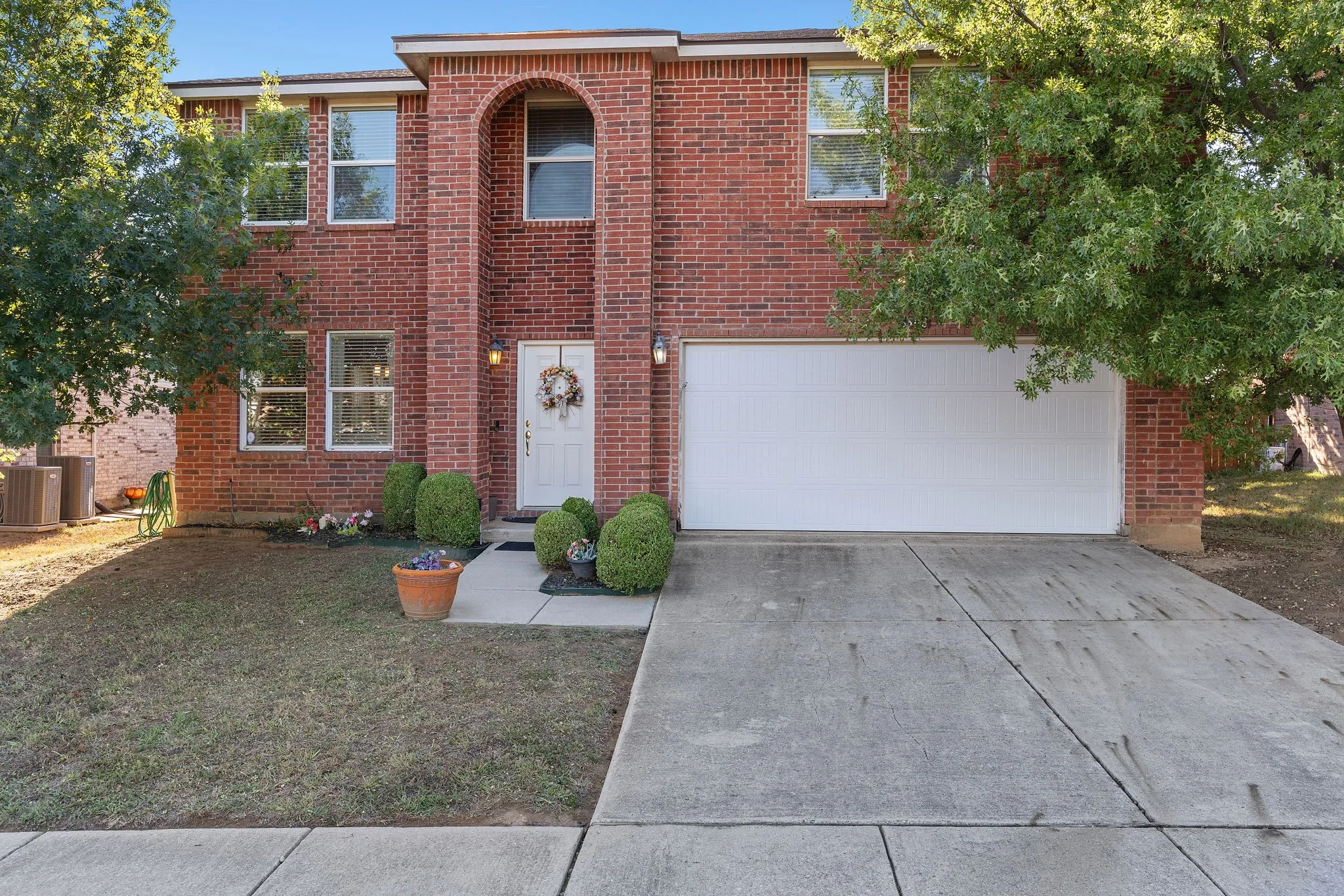 Red brick exterior featuring an arched entry, multiple windows, a white front door, and an attached garage