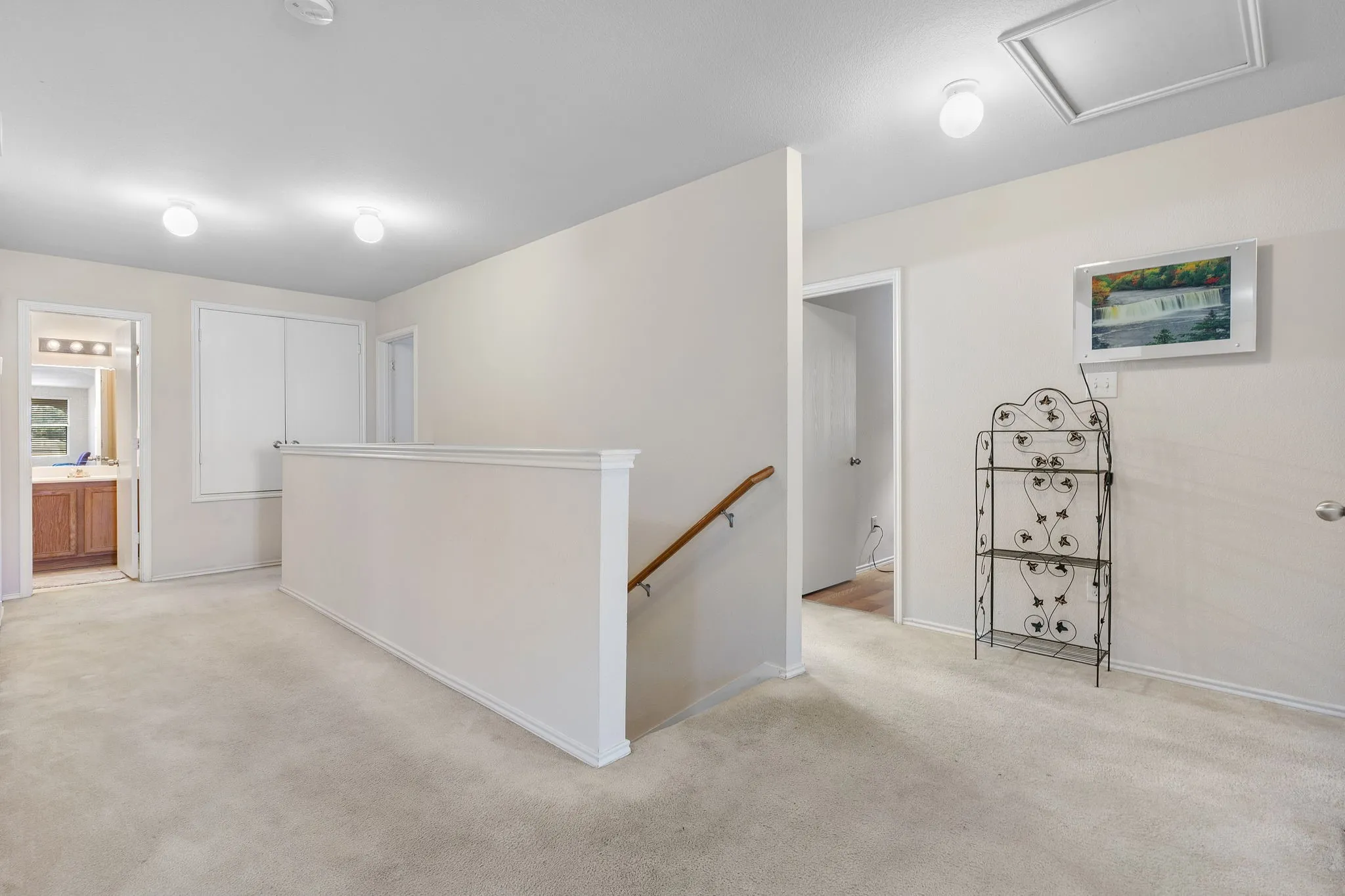 Carpeted landing area featuring a white railing, flush mount ceiling lights, and an attic access panel