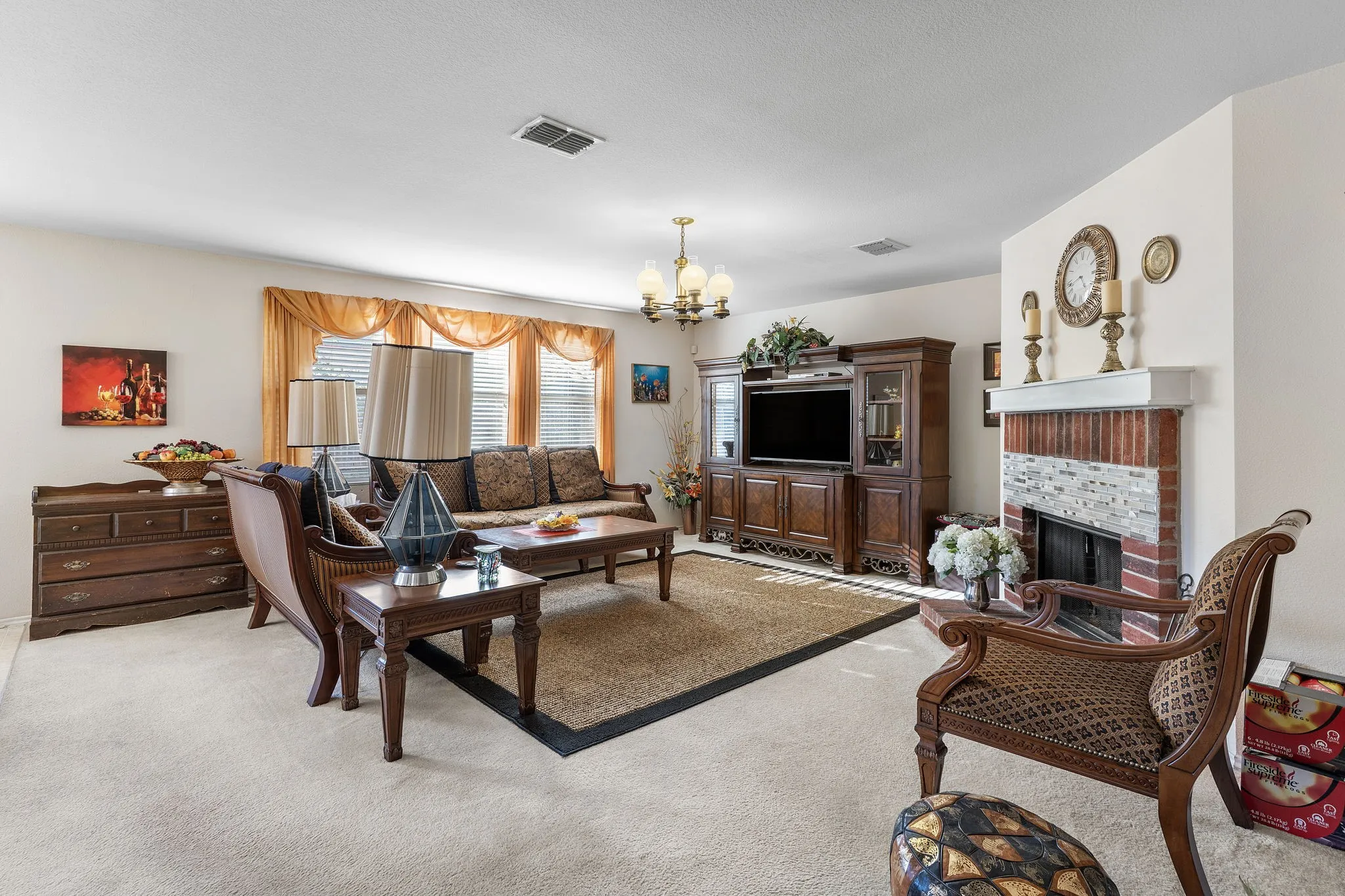 Carpeted living space featuring a fireplace with brick and tile surround, a built-in entertainment center, and a chandelier