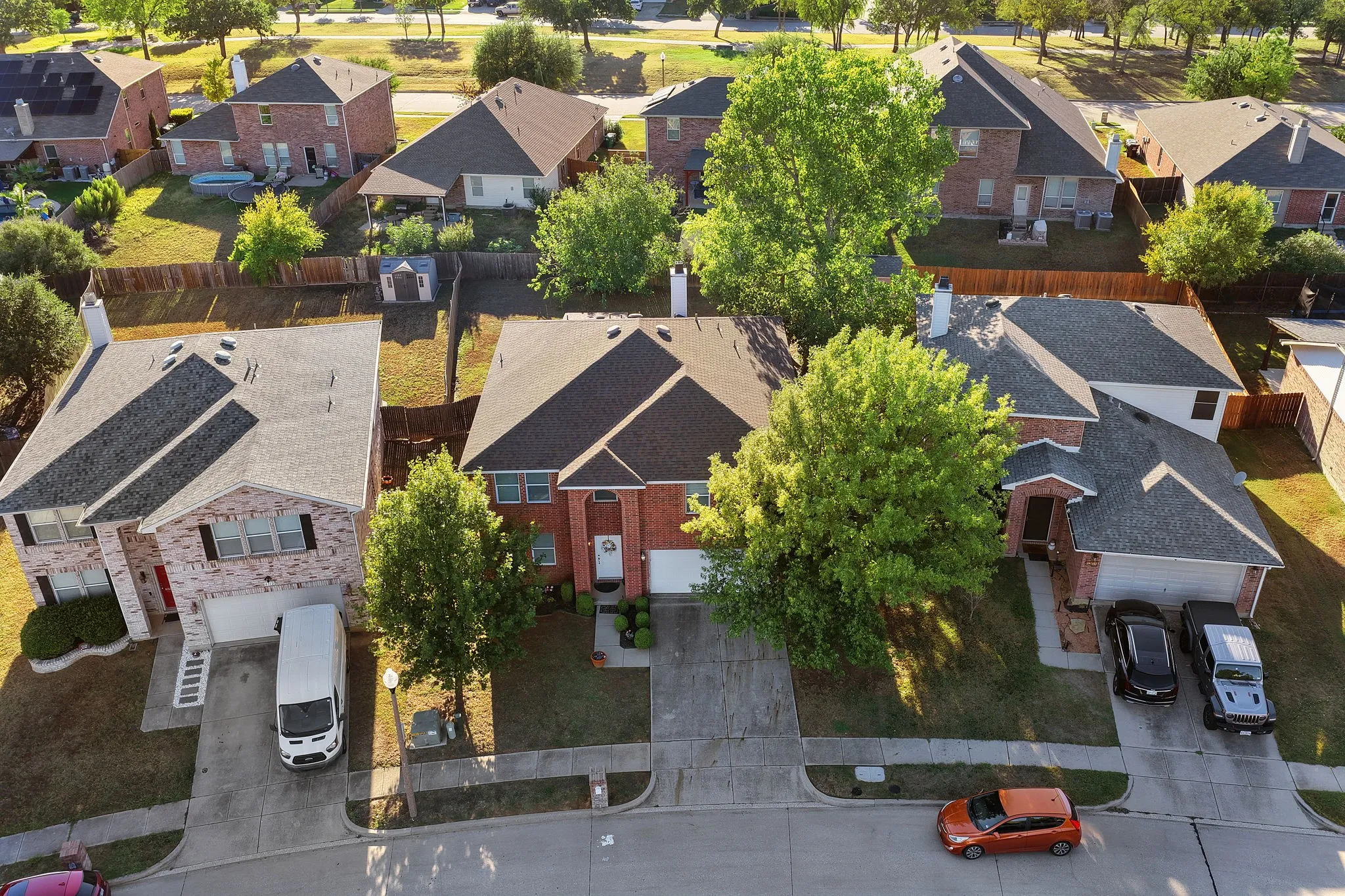 Brick exterior with a gabled roofline, mature trees, and a concrete driveway