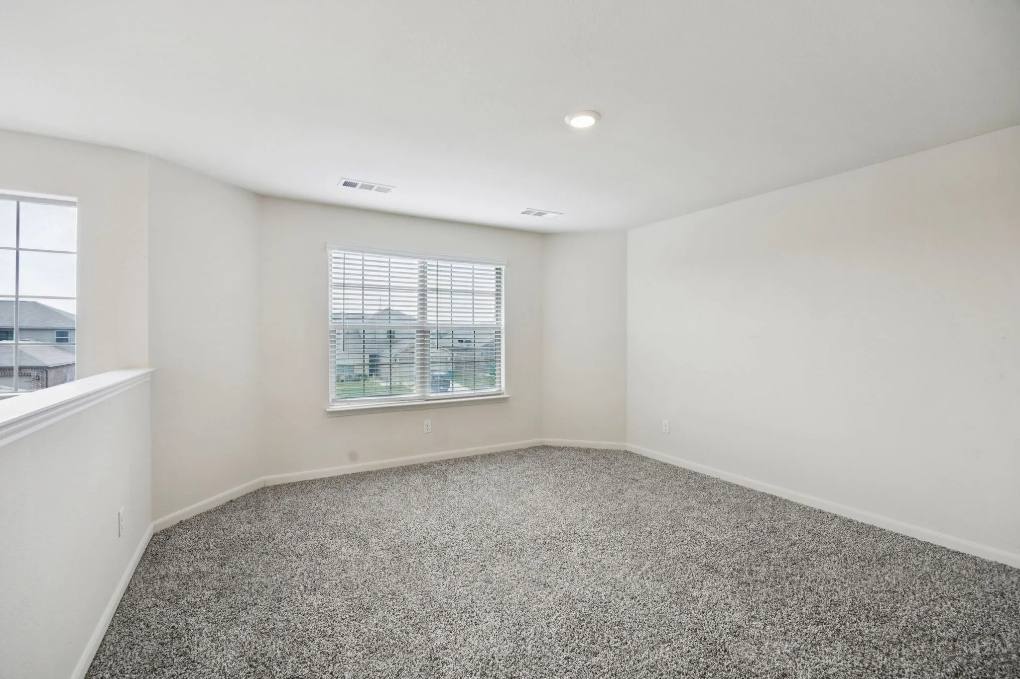 Expansive carpeted area featuring two windows with blinds, a half-wall partition, and recessed ceiling lighting