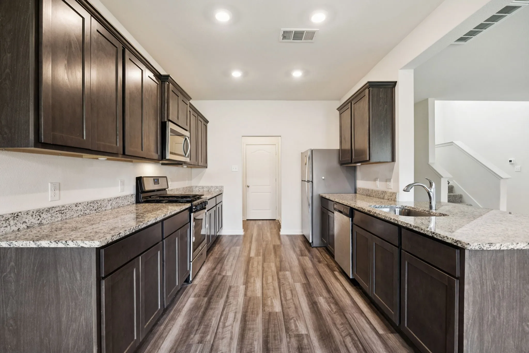 Galley kitchen featuring wood-finish flooring, dark wood cabinetry, light stone countertops, and stainless steel appliances