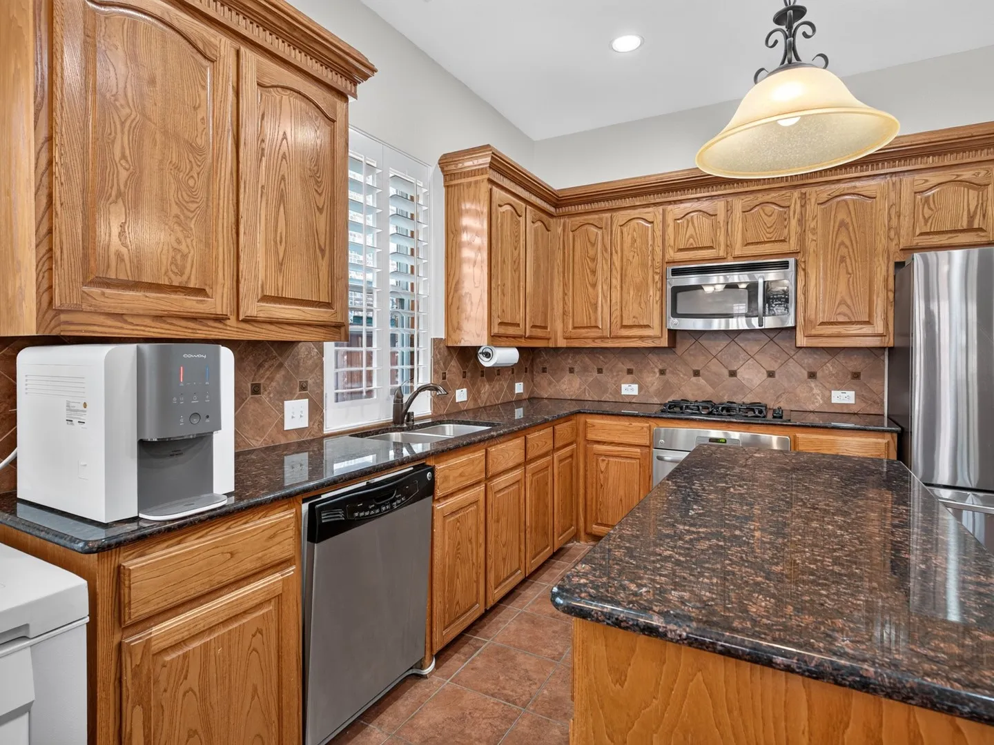 Wood-finish cabinetry with crown molding, dark speckled countertops, stainless steel appliances, and a tiled backsplash