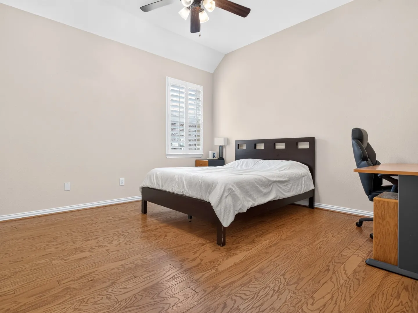 Vaulted ceiling, wood-finish flooring, white plantation shutters, and a ceiling fan with integrated lighting