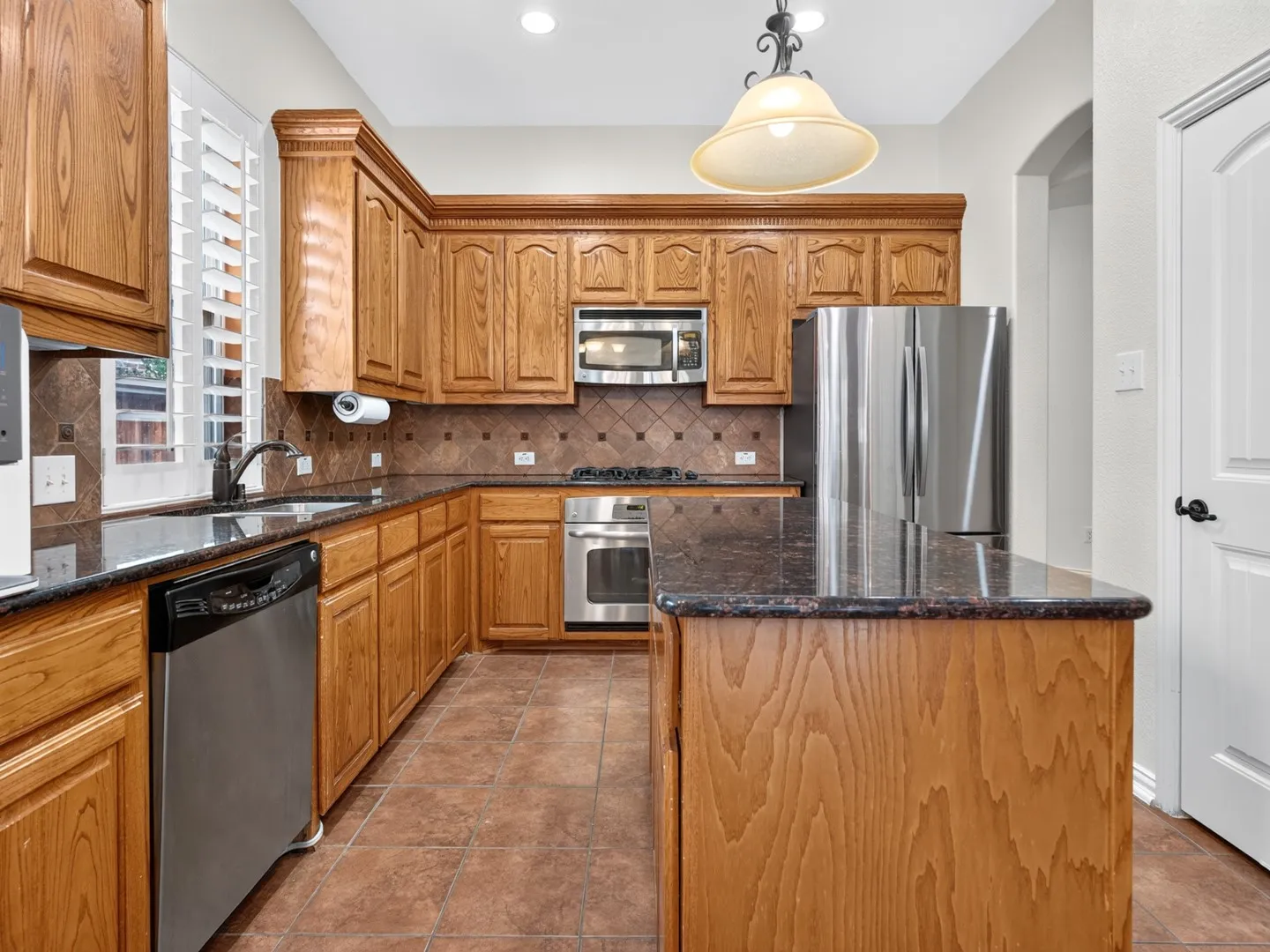 Wood cabinetry with crown molding, stainless steel appliances, dark stone countertops, tile backsplash, and tile flooring
