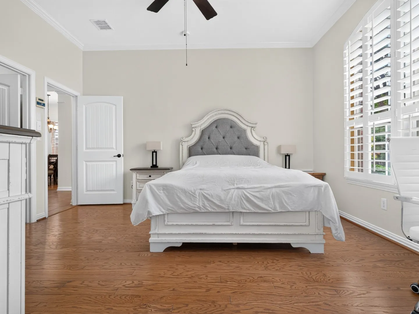 Wood-finish flooring throughout, arched window with plantation shutters, ceiling fan, and crown molding