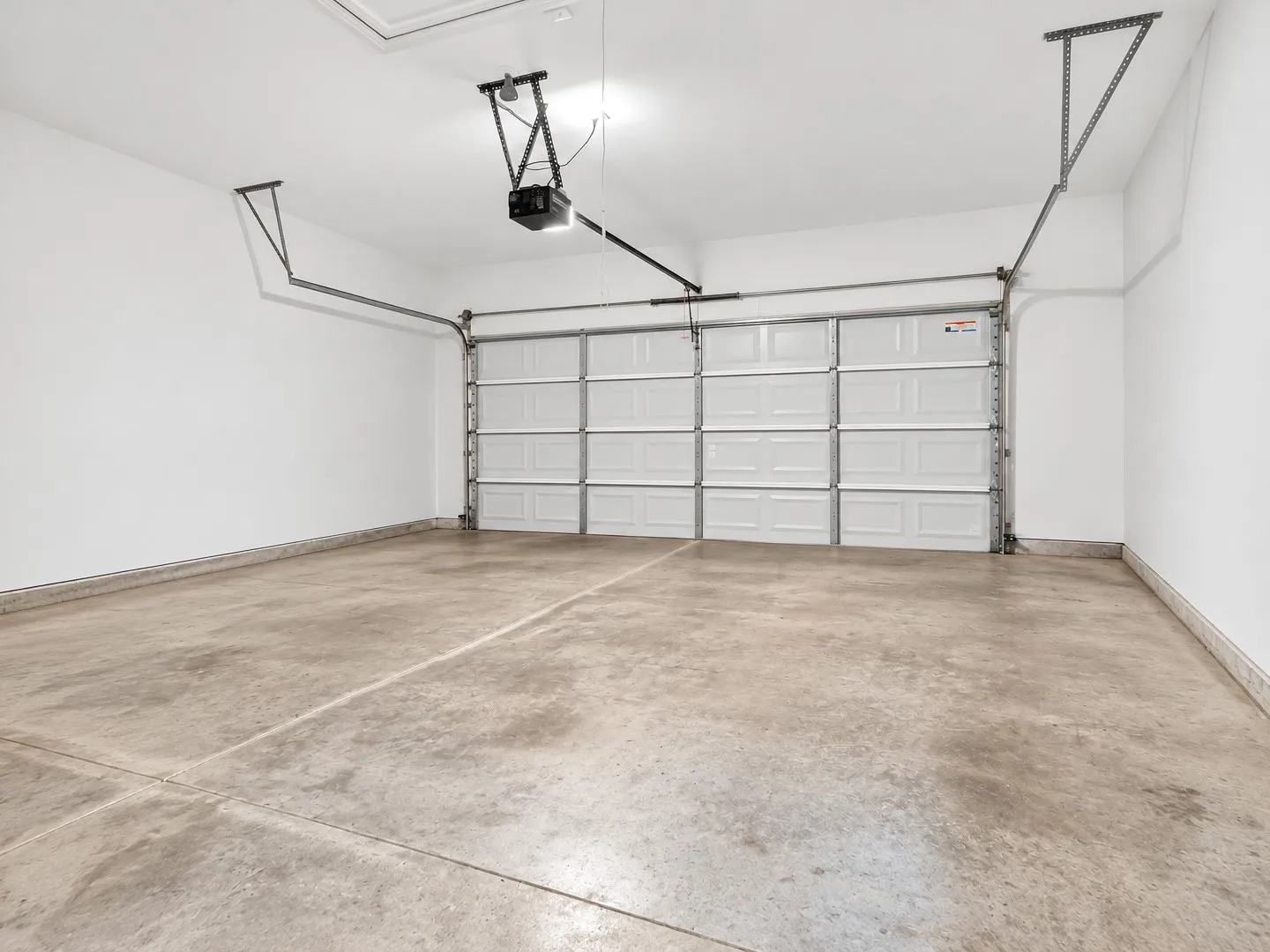 Concrete flooring with a segmented overhead garage door, equipped with an automatic opener