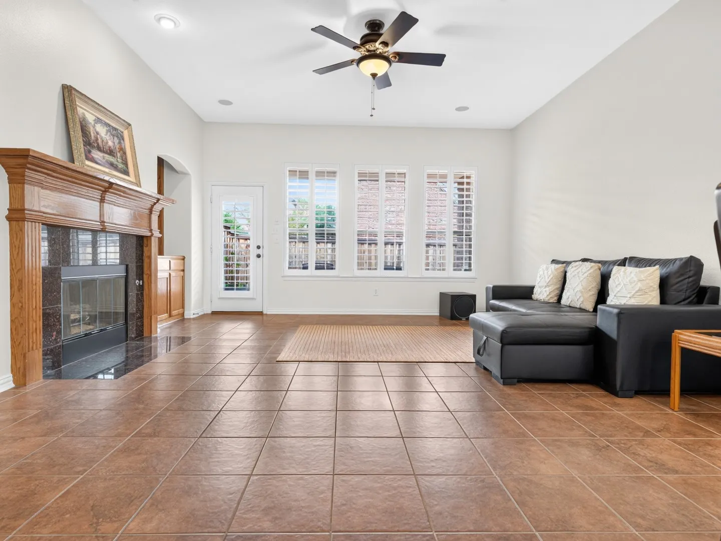 Vaulted ceilings with recessed lighting, an ornate wood-mantle fireplace with a dark stone surround, tiled flooring, a ceiling fan, and multiple windows with plantation shutters