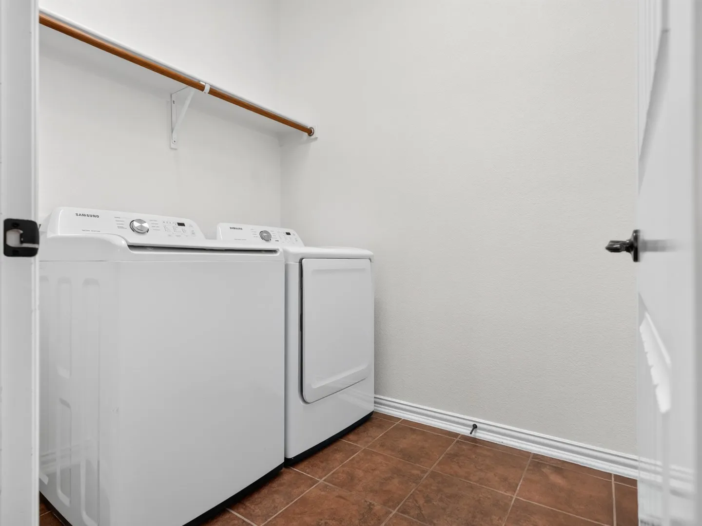 Dedicated laundry space featuring a hanging rod and terracotta-style floor tiles