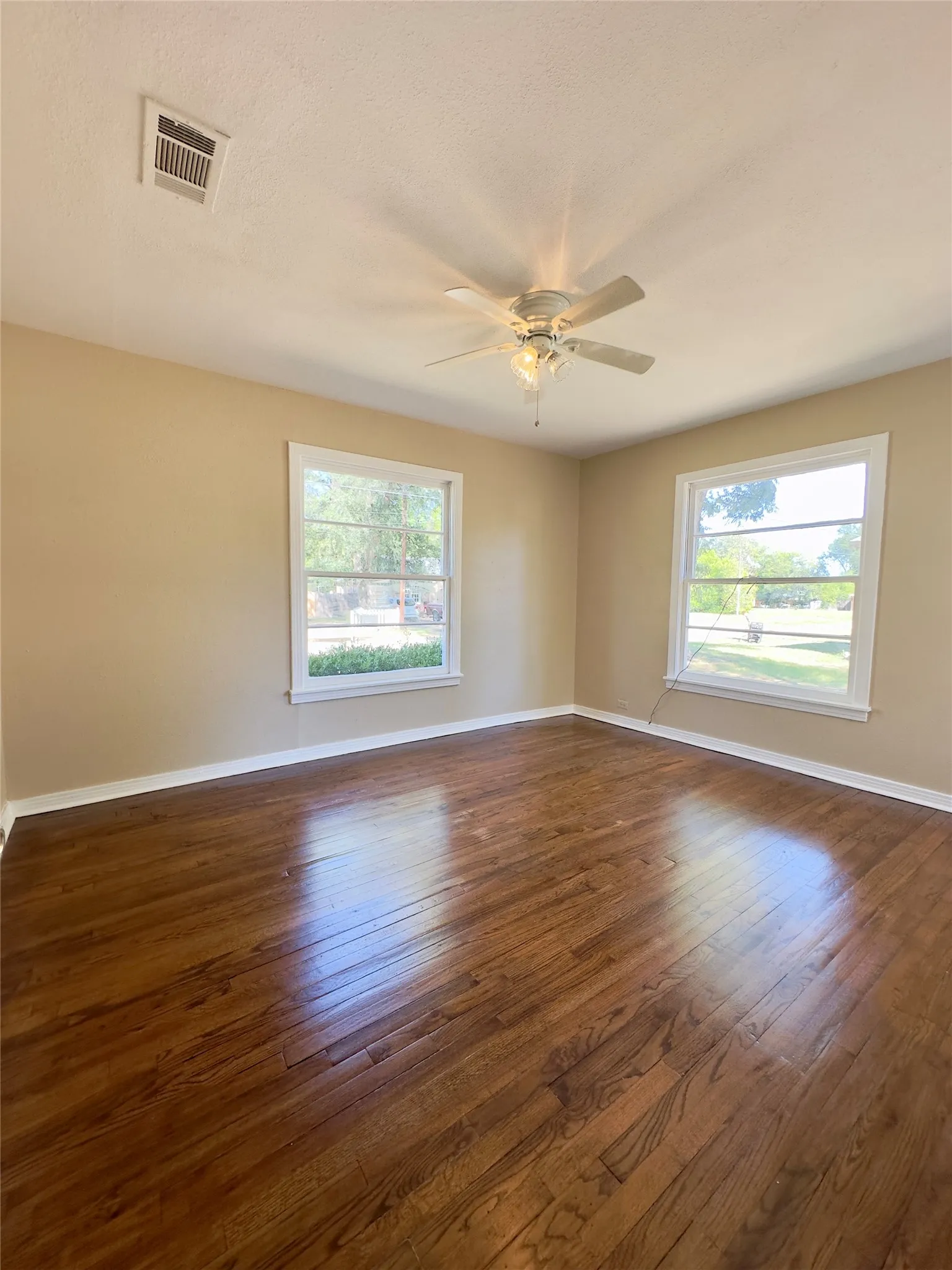 Rich wood-finish flooring, dual windows with white trim, and a ceiling fan with integrated lighting