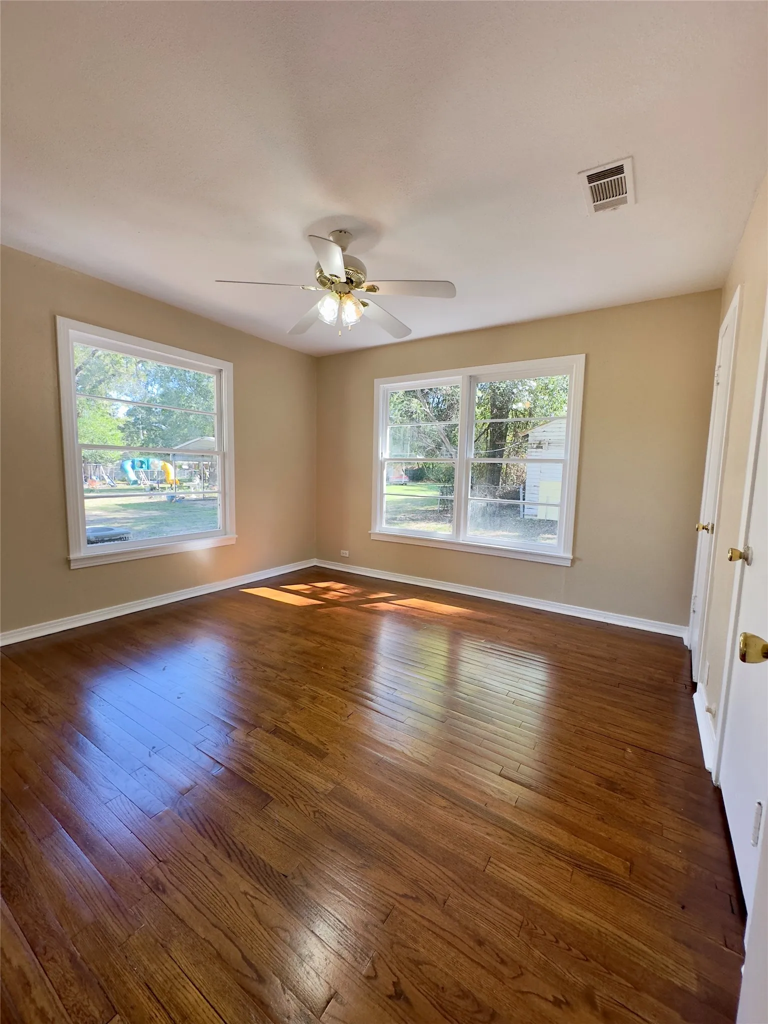 Hardwood flooring, two windows with white trim, ceiling fan, and painted walls