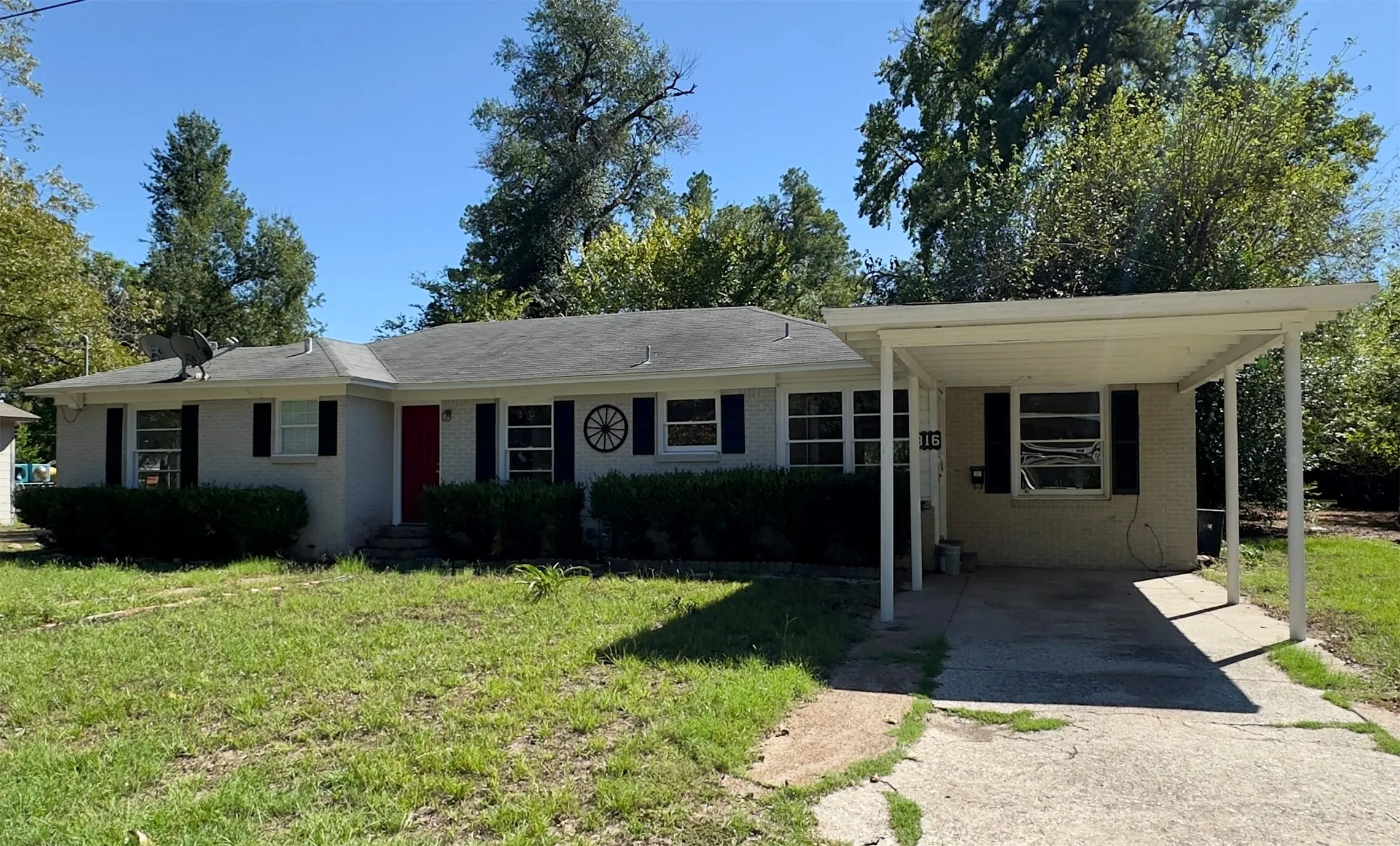 Single-story residence with a gray exterior, black window shutters, a red entry door, and an attached carport
