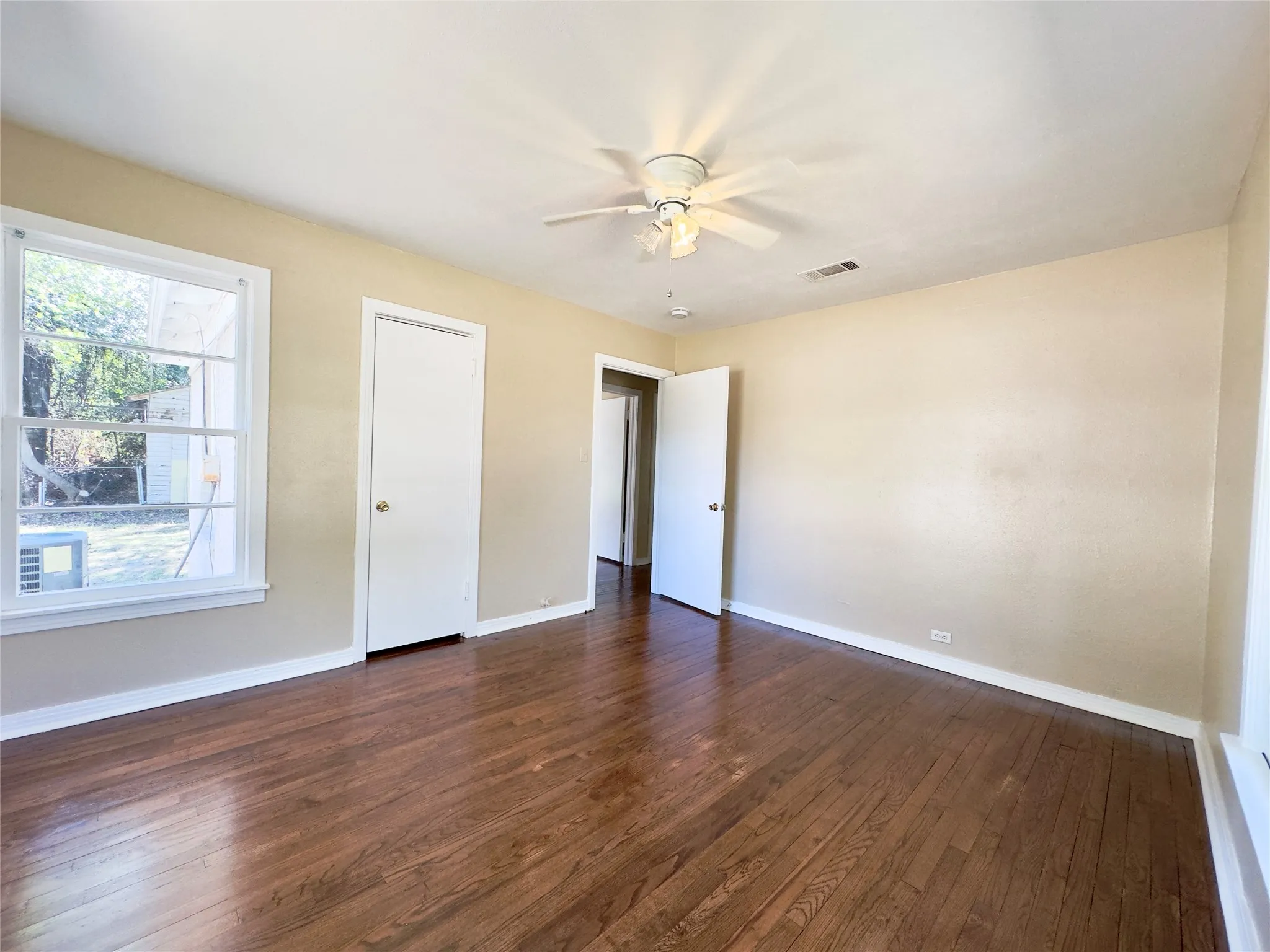 Hardwood flooring, painted walls, ceiling fan with integrated lighting, multiple windows, and a doorway with a panel door