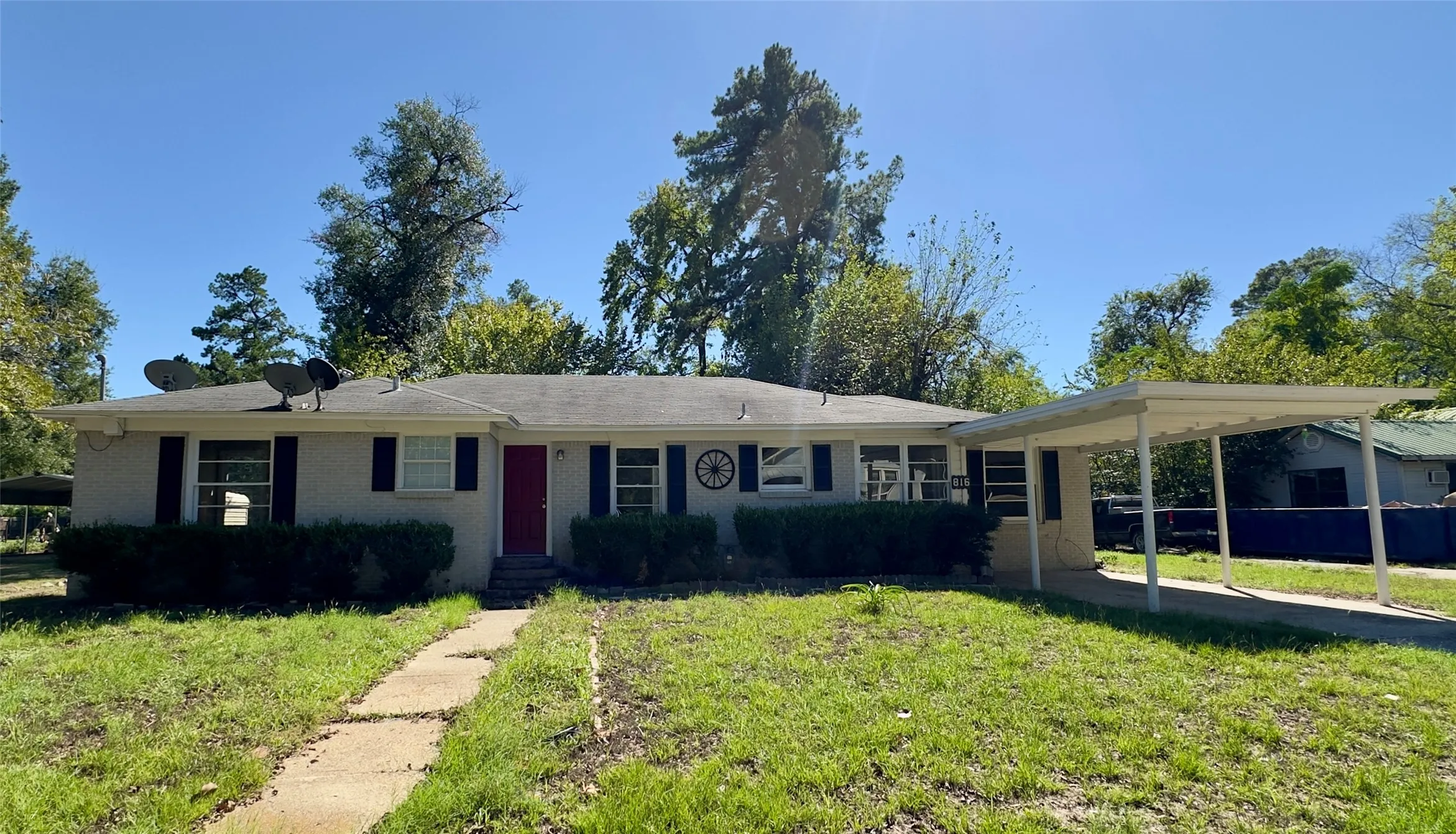 Single-story exterior with a red entry door, white trim, and a covered carport