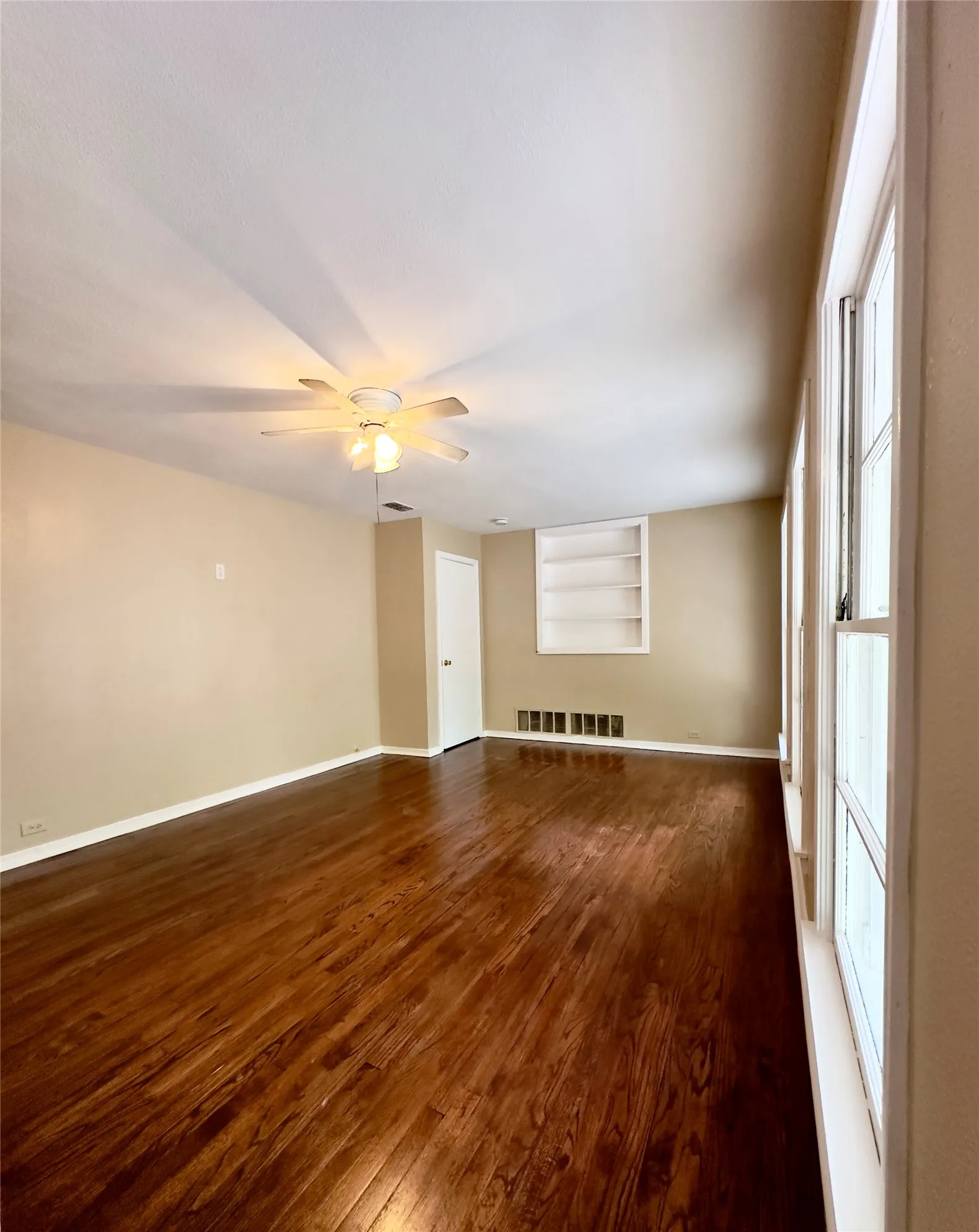 Hardwood flooring, multiple windows, ceiling fan with integrated lighting, built-in shelving, and a white door