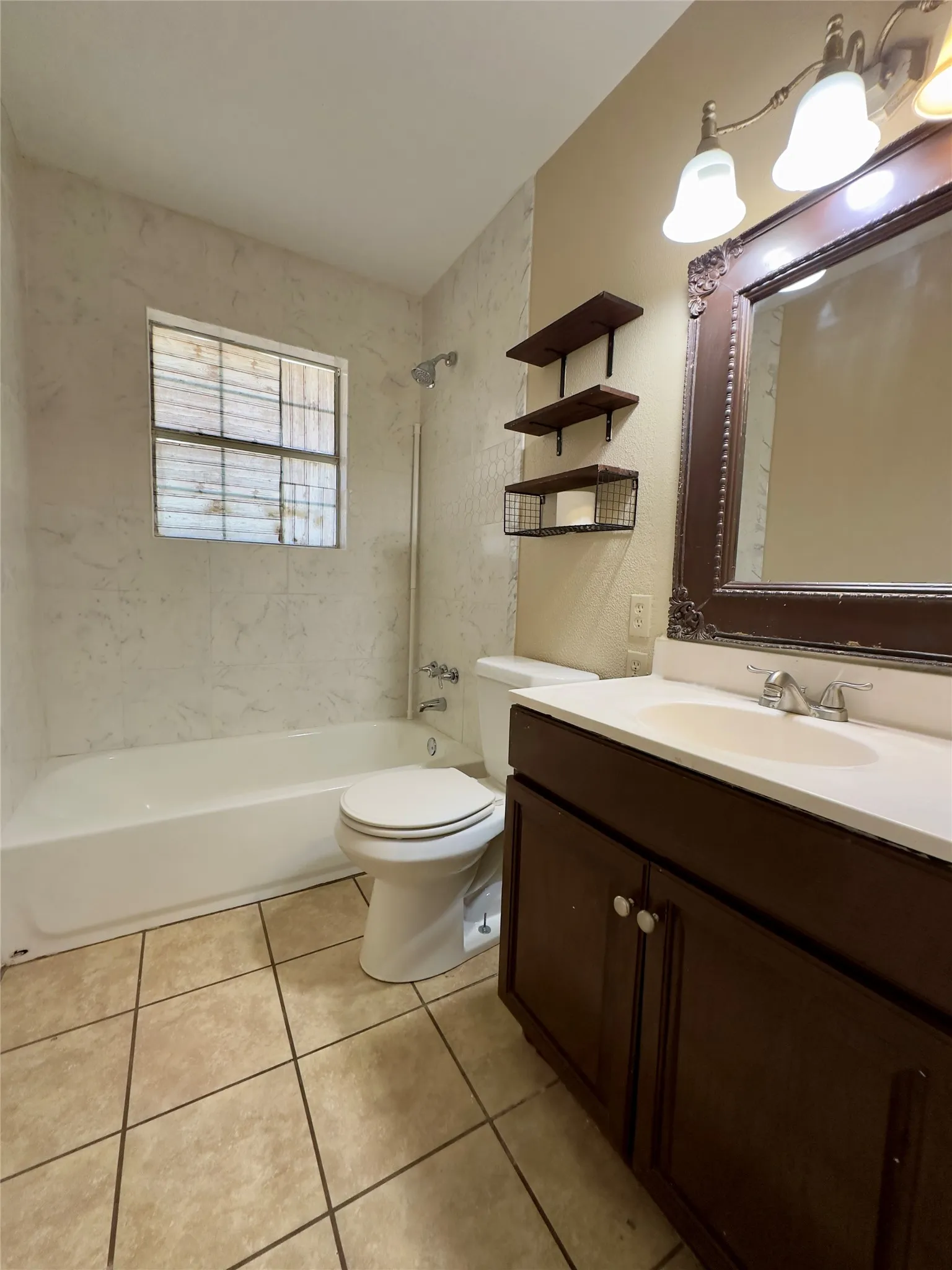 White bathtub with tile surround, dark wood-finish vanity with white countertop, chrome faucet, and tiled flooring