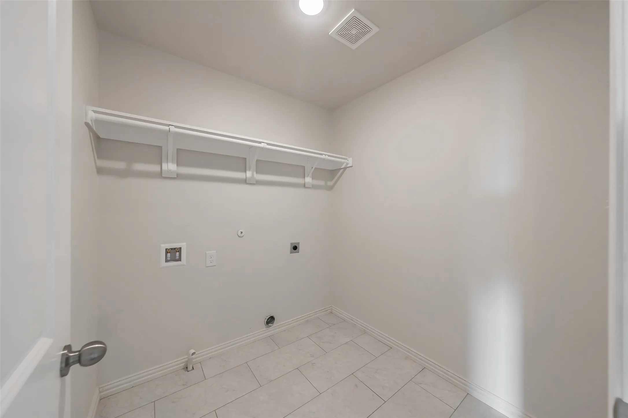 Washroom with washer hookup, electric dryer hookup, light tile patterned floors. Long shelve for storage and rod to hang clothing.