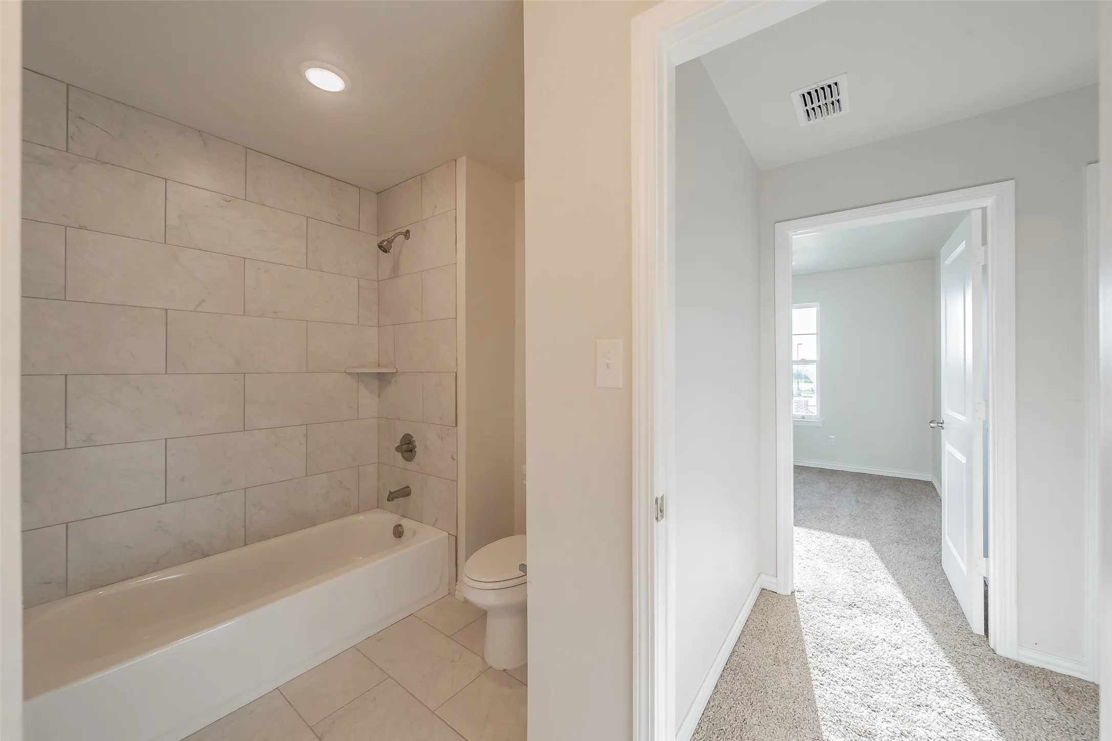  Hallway Bathroom with tiled shower / bath combo, tile patterned flooring, and toilet