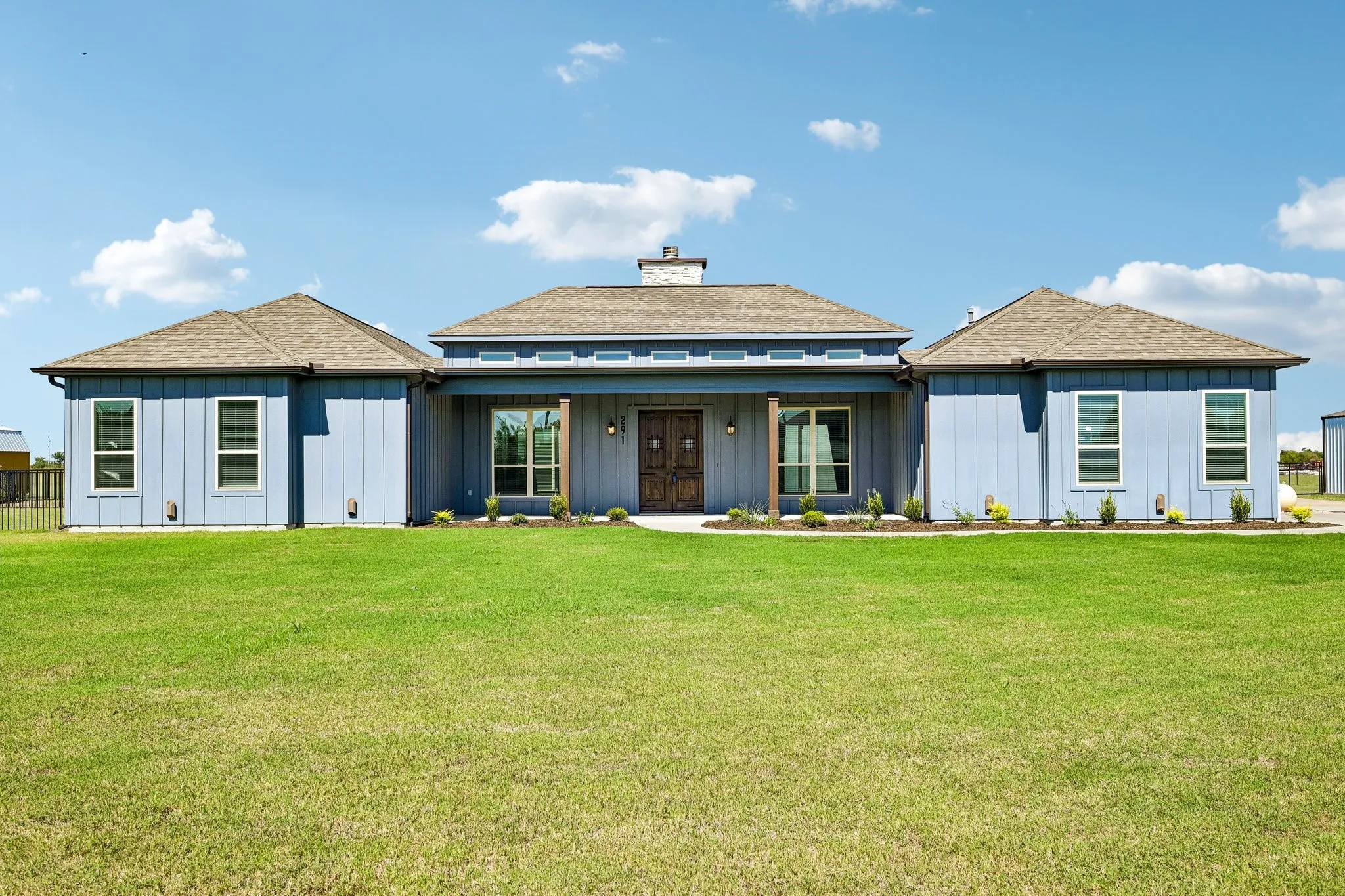 Light blue vertical siding exterior, wood-finish columns, double entry doors, multiple windows, and a shingle roof