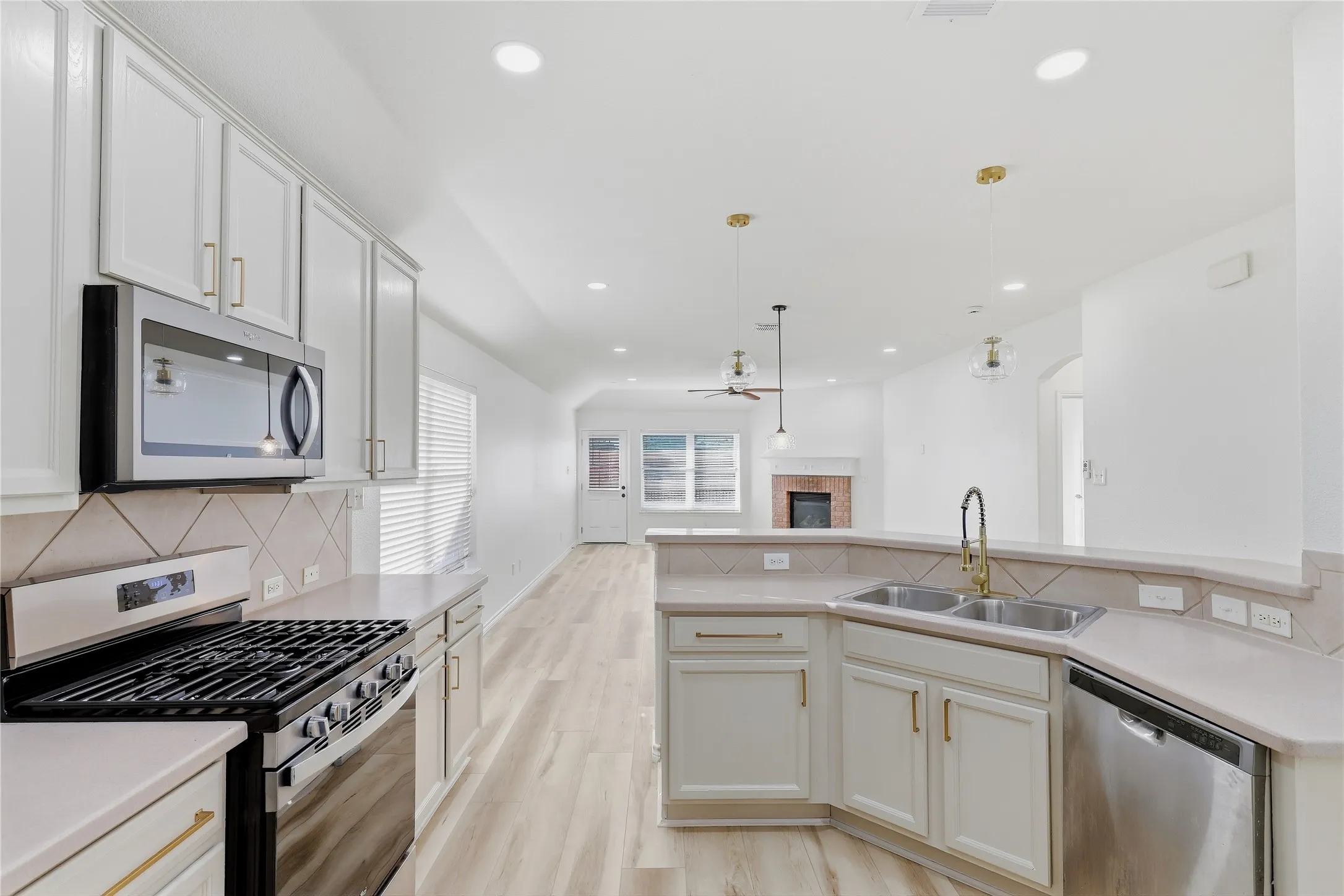 Light-toned kitchen cabinetry with gold-finish hardware, stainless steel appliances, and a double basin sink