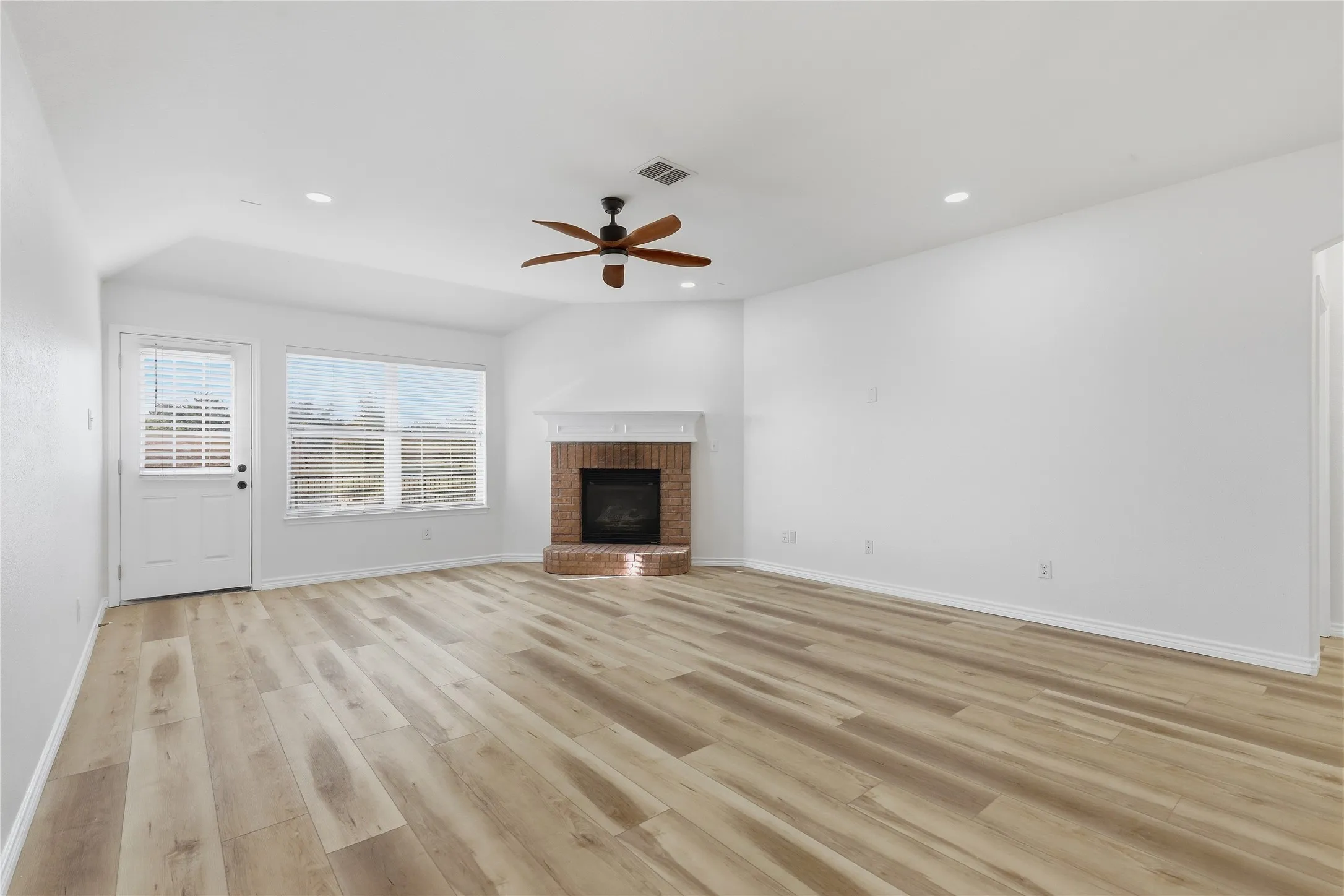 Spacious living area featuring wood-finish flooring, a brick fireplace, and a ceiling fan