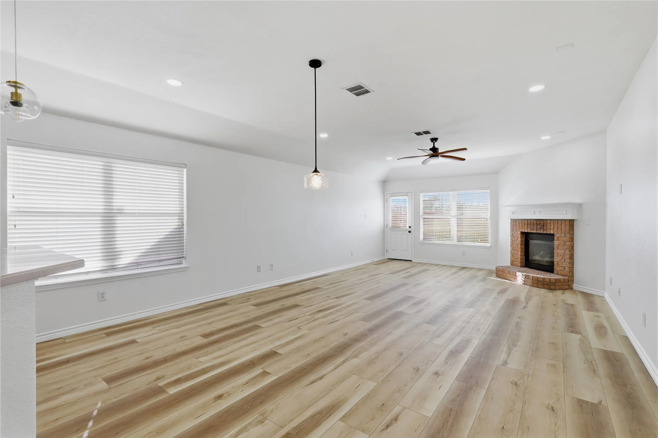 Spacious room featuring wood-finish flooring, a brick fireplace with a mantle, a ceiling fan, and recessed lighting