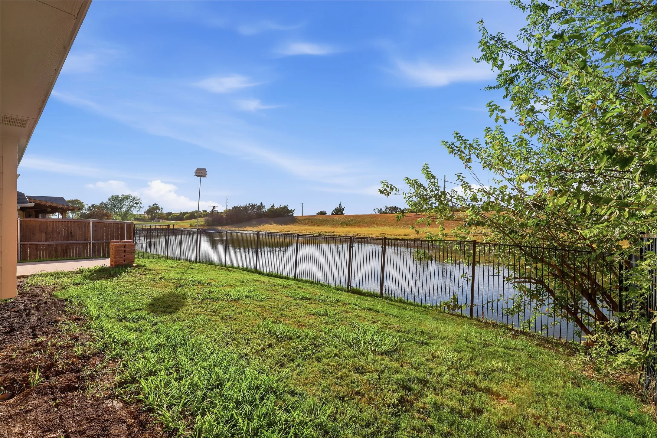 Expansive backyard featuring a manicured lawn, a black metal fence, and a water feature