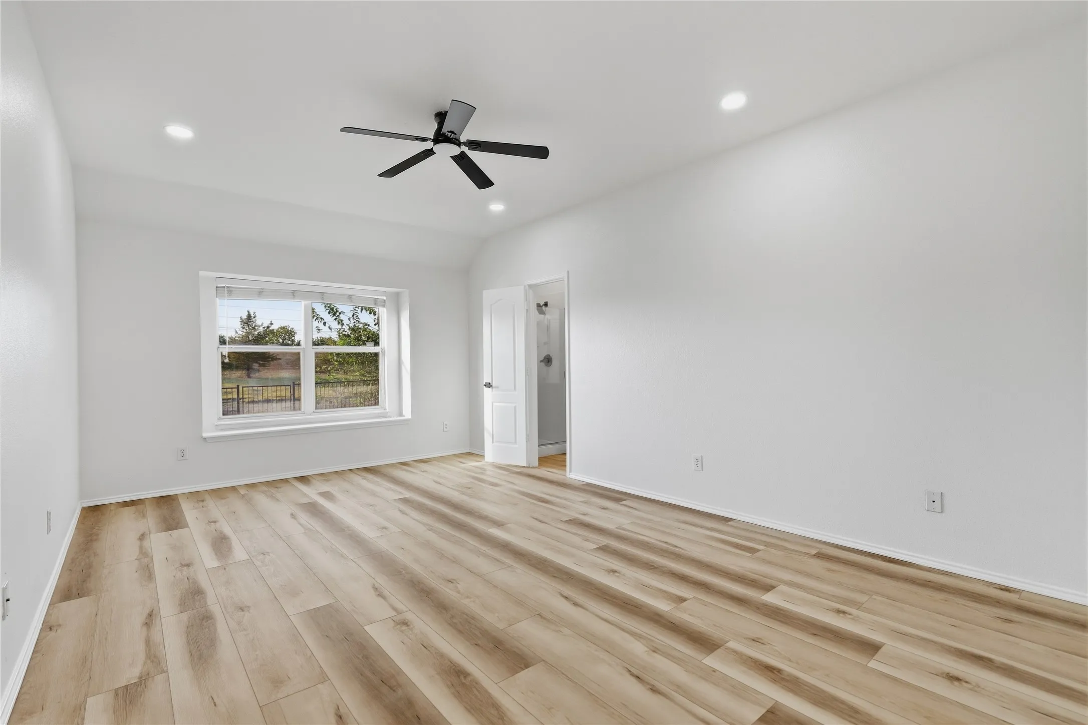 Spacious room featuring wood-finish flooring, a large window, a ceiling fan with integrated lighting, and recessed ceiling lights