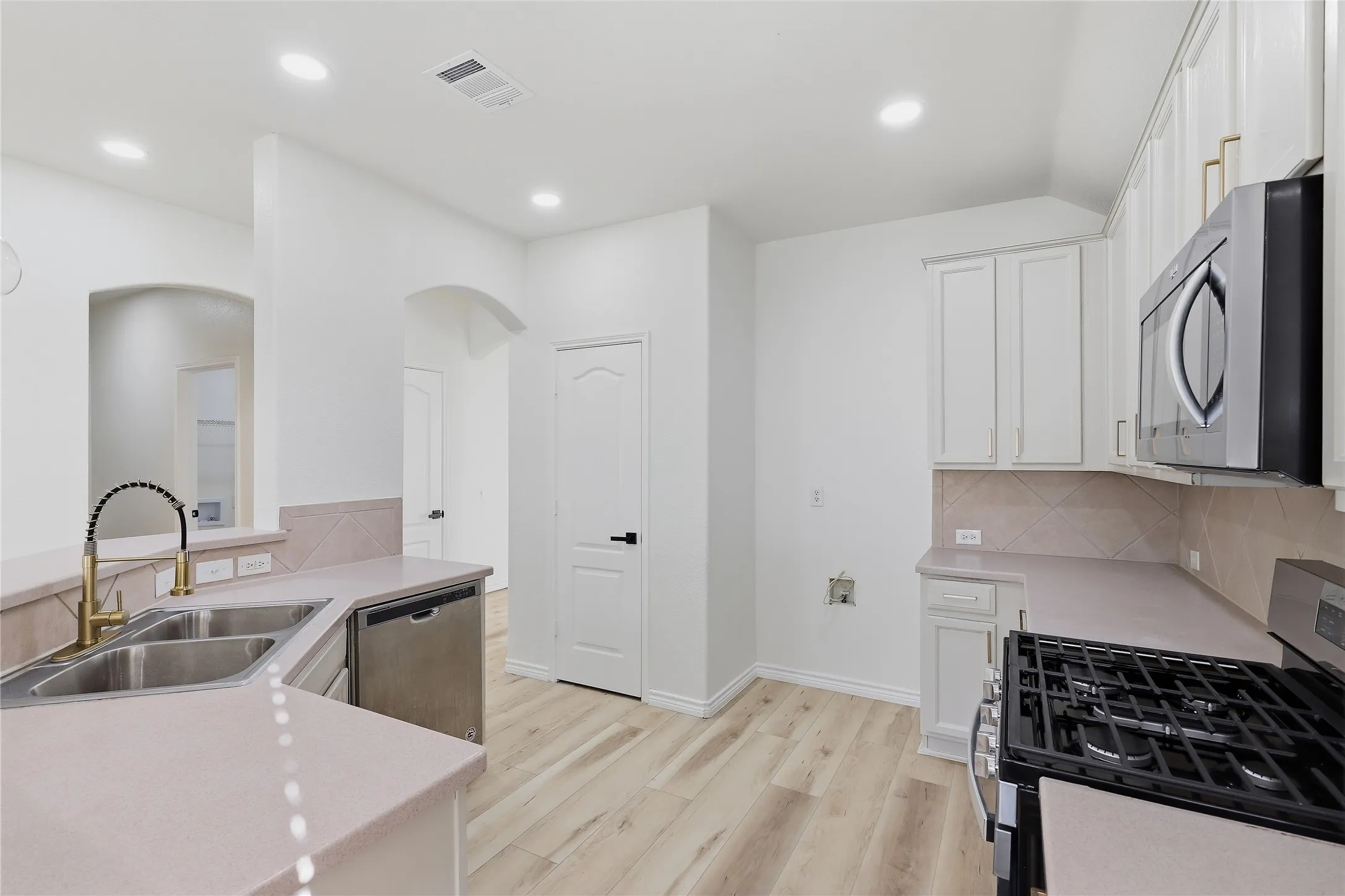Kitchen featuring wood-finish flooring, recessed lighting, white cabinetry, a stainless steel gas range, and a dual basin sink with a gold-finish faucet