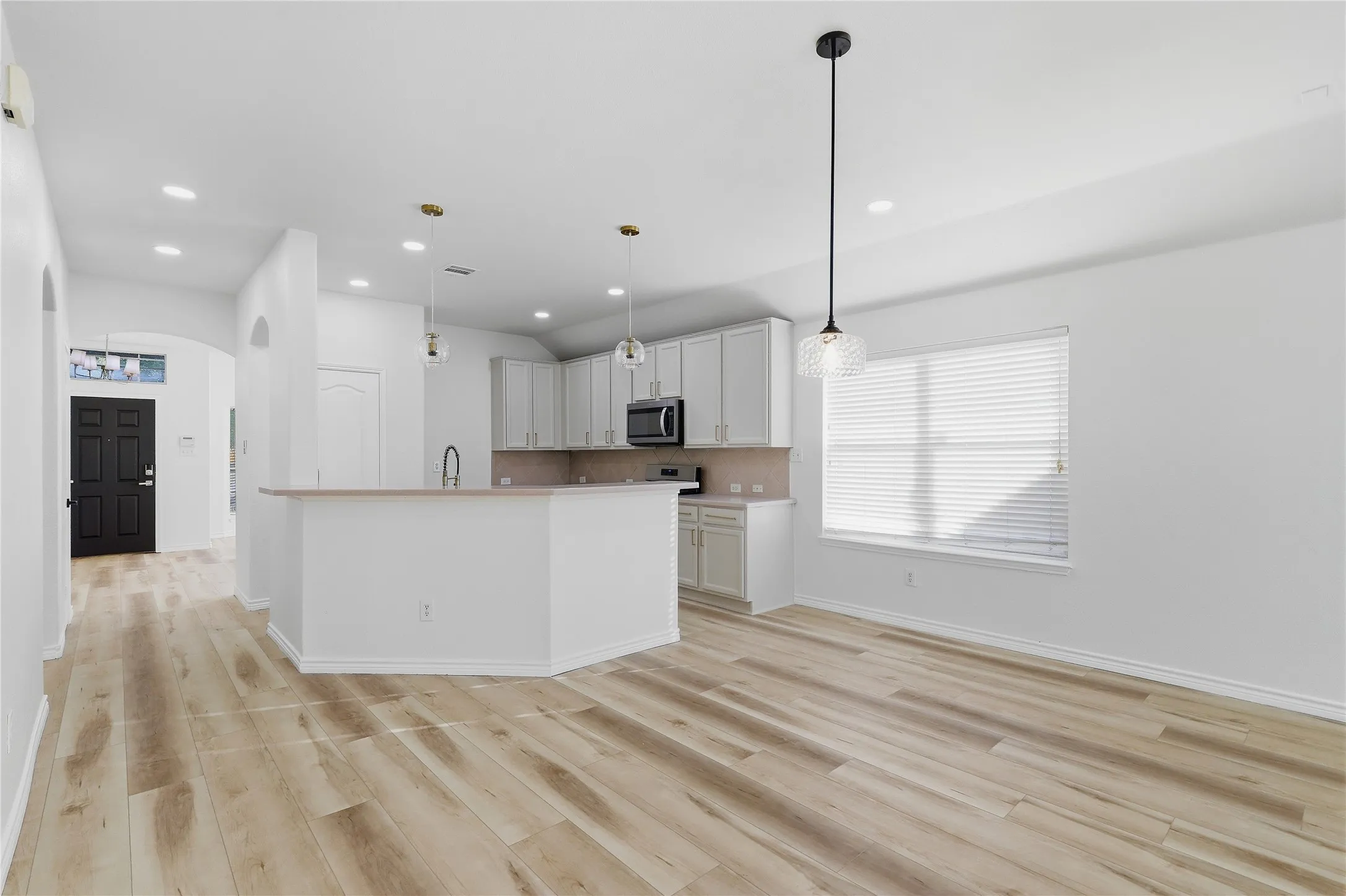 Wood-finish flooring, recessed lighting, sleek pendant lights, light-toned cabinetry, and stainless steel appliances