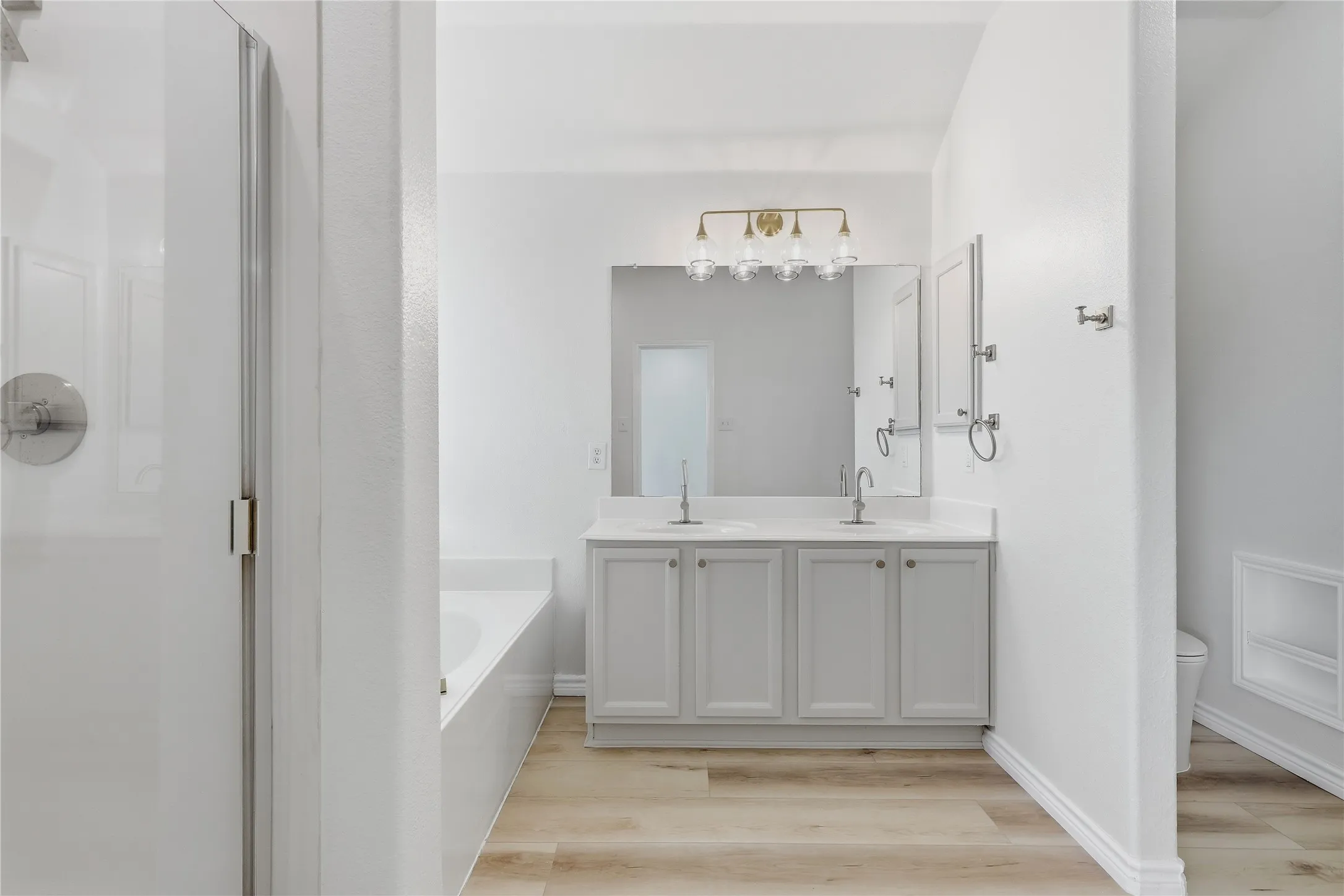 Dual sink vanity with light gray cabinetry, wall-mounted mirror, and gold-finish vanity lighting