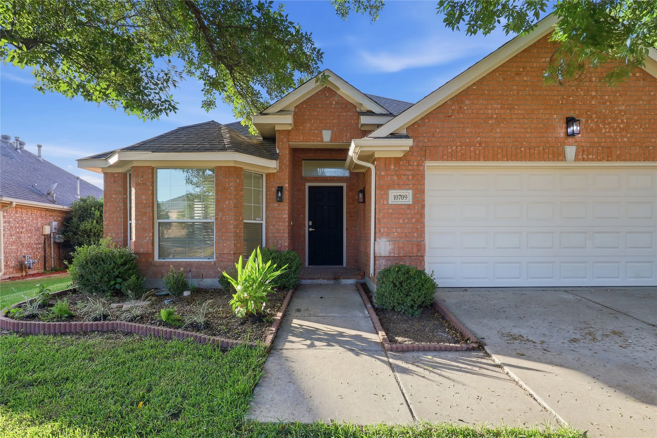 Brick facade with a white garage door, concrete walkway, and landscaped front garden