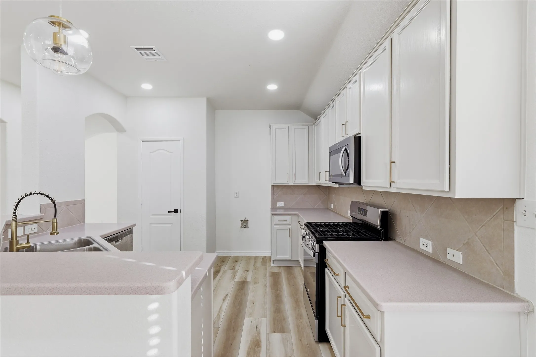 Modern kitchen featuring light wood-finish flooring, white cabinetry with gold-tone hardware, a stainless steel microwave, and a black gas range
