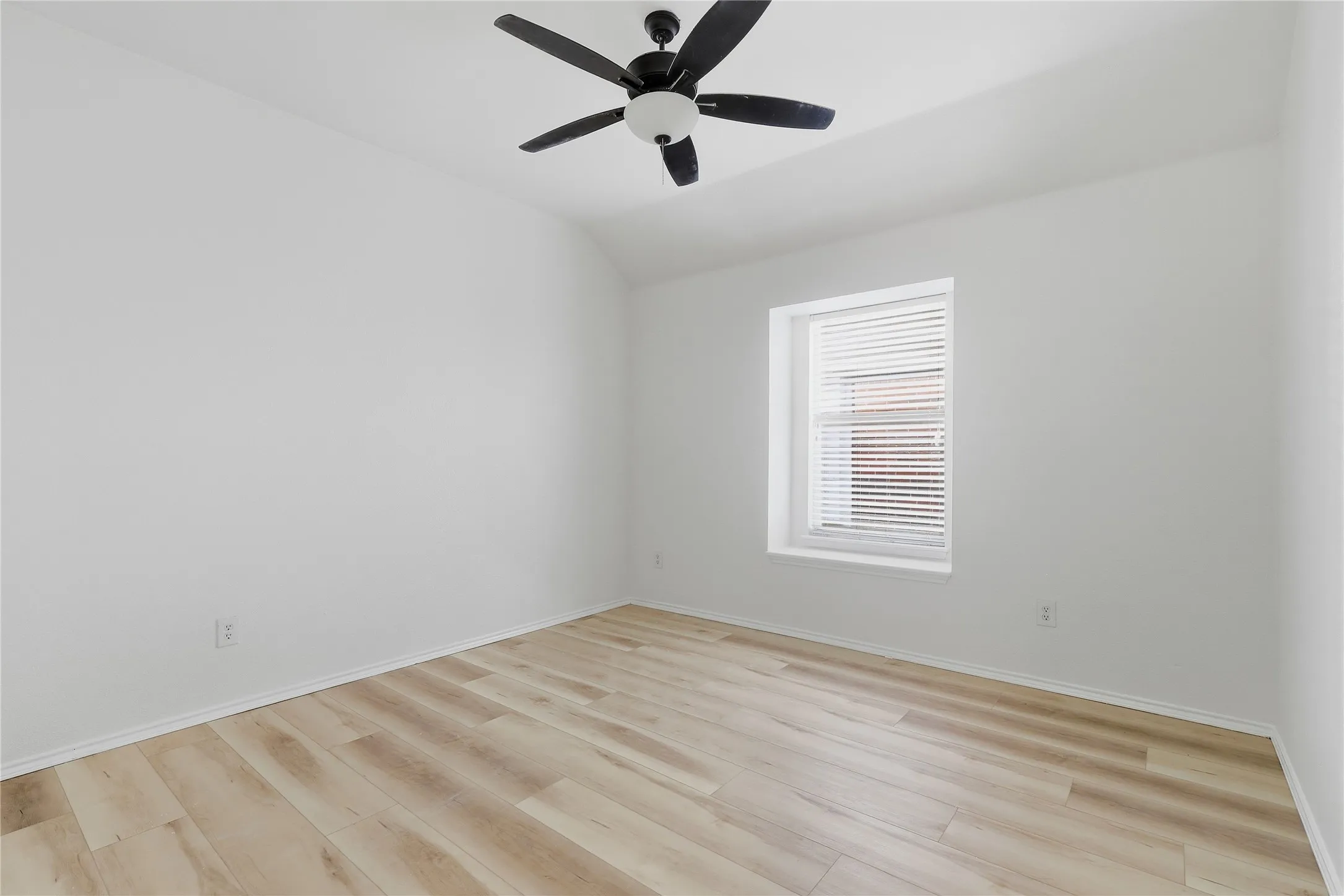 Light wood-finish flooring with white walls and trim, featuring a recessed window with blinds and a ceiling fan with integrated lighting