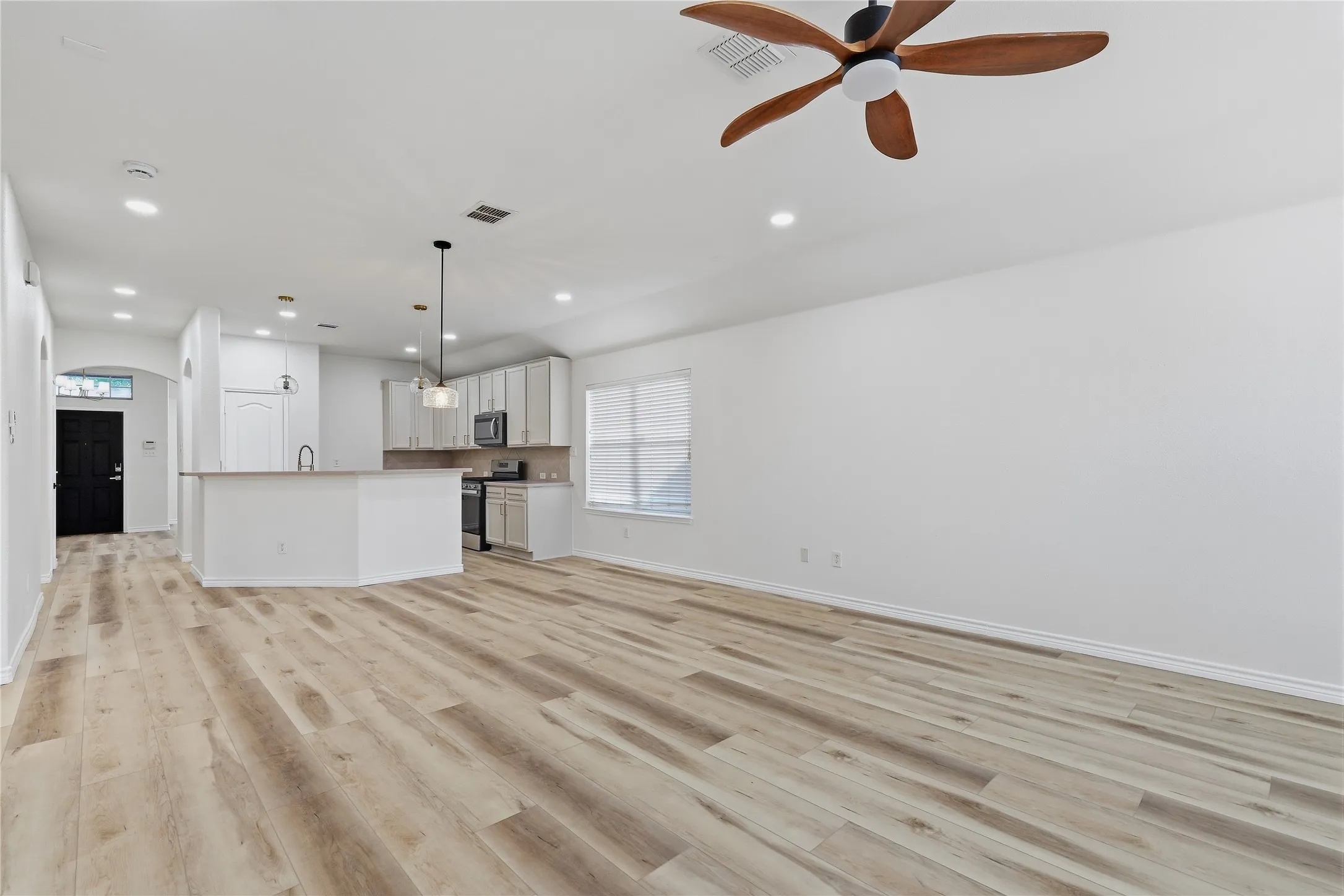 Open-concept living area featuring wood-finish flooring, recessed lighting, a modern ceiling fan, and a kitchen island with pendant lighting