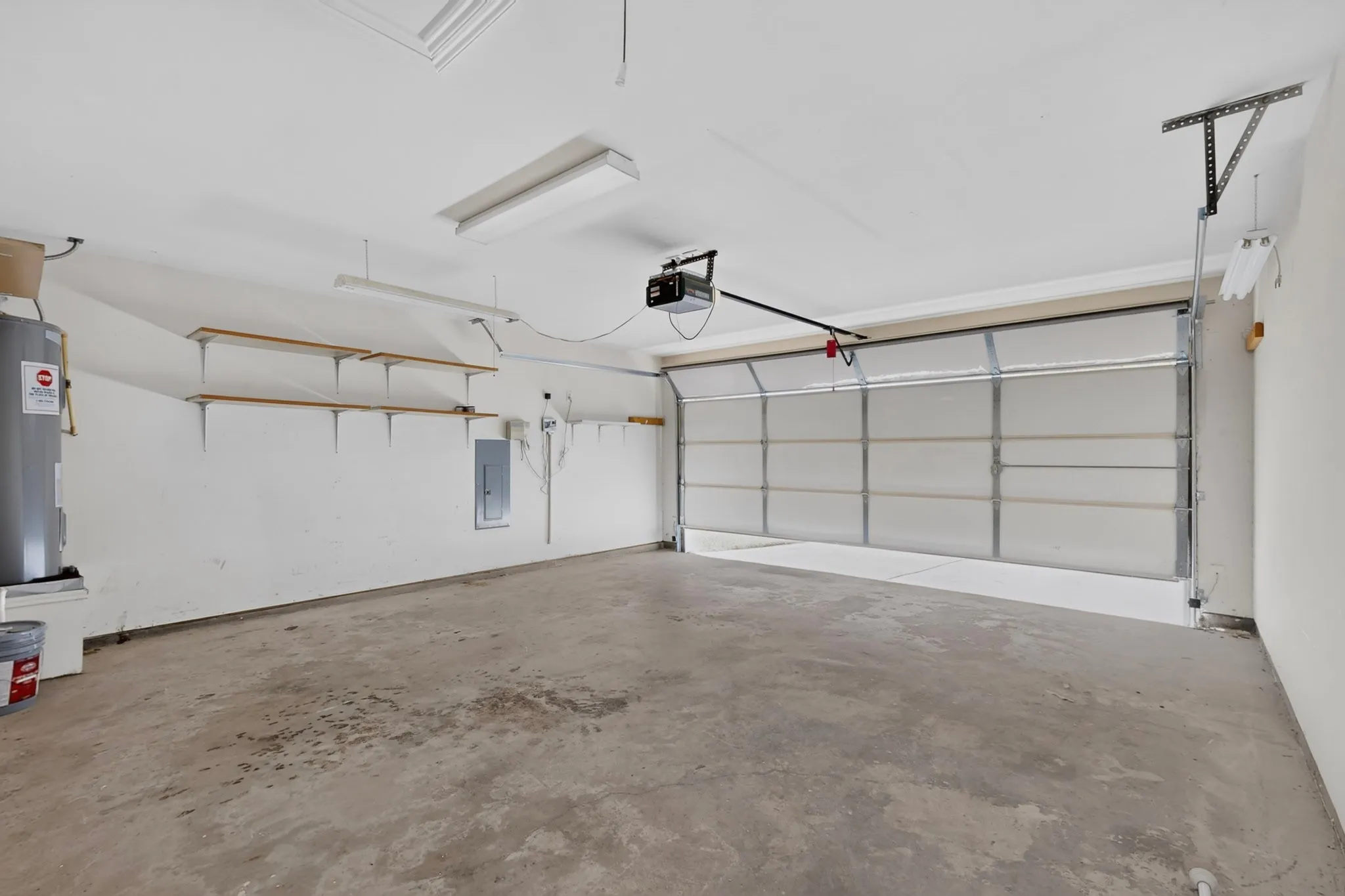 Concrete flooring with automatic garage door opener, overhead lighting, and built-in shelving