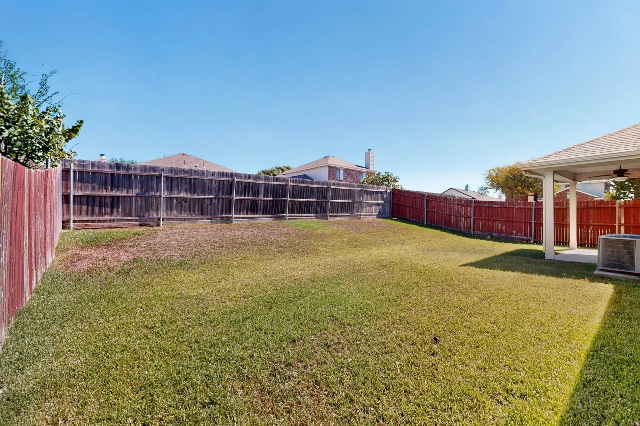 Expansive fenced backyard with a covered patio, ceiling fan, and concrete flooring