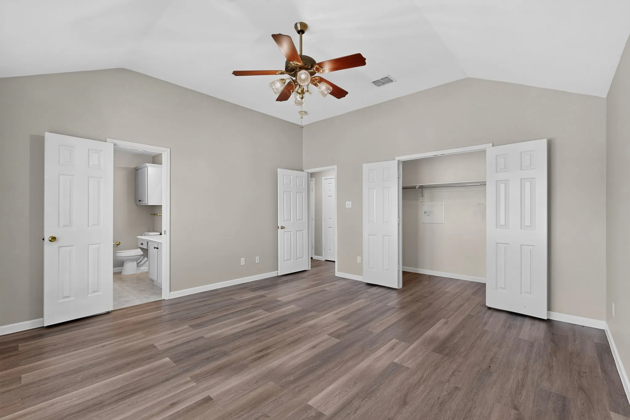 Vaulted ceilings with a ceiling fan, wood-finish flooring, and a walk-in closet with bi-fold doors