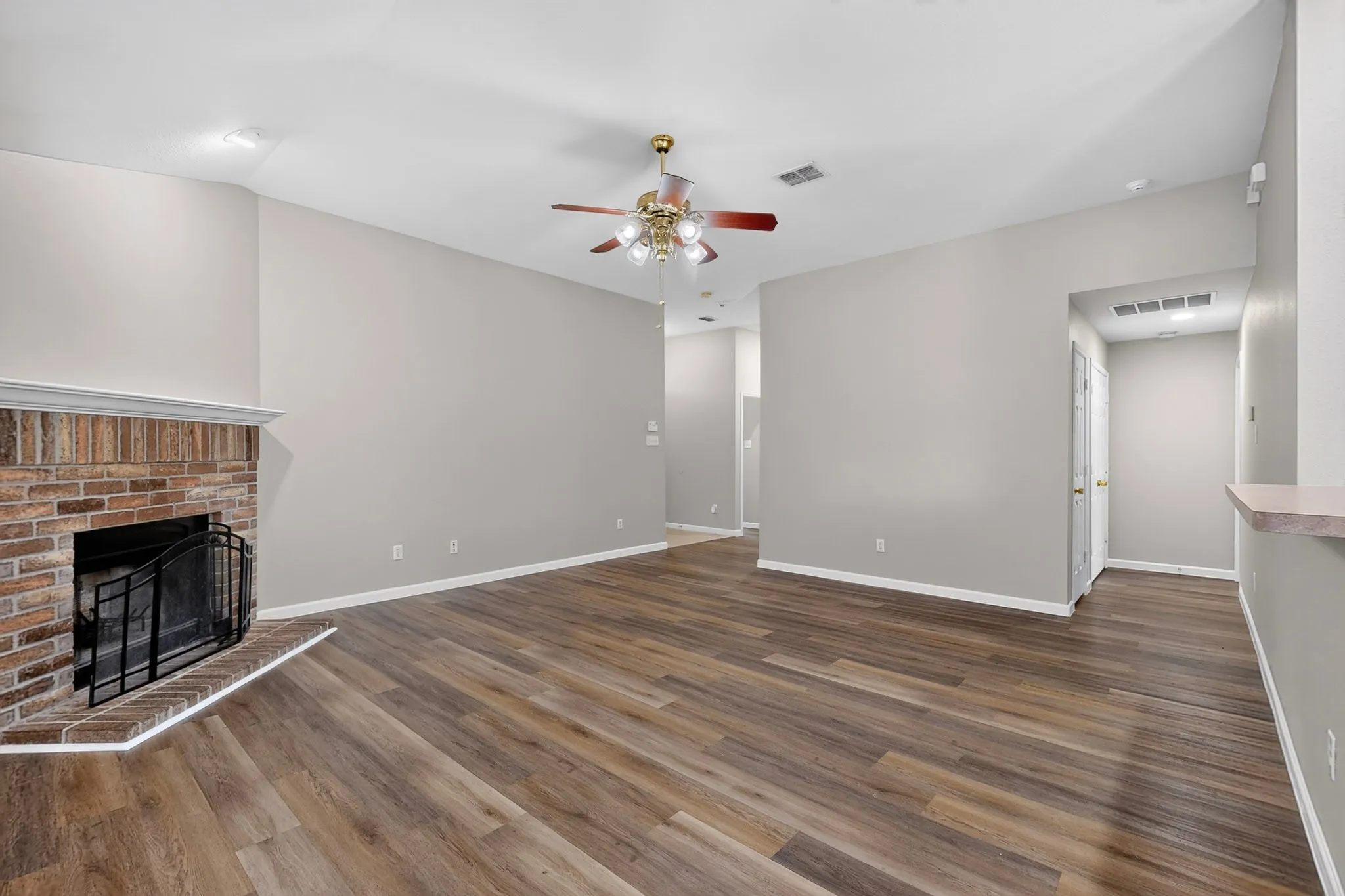 Spacious room featuring wood-finish flooring, a brick fireplace with a hearth, a ceiling fan, and recessed lighting