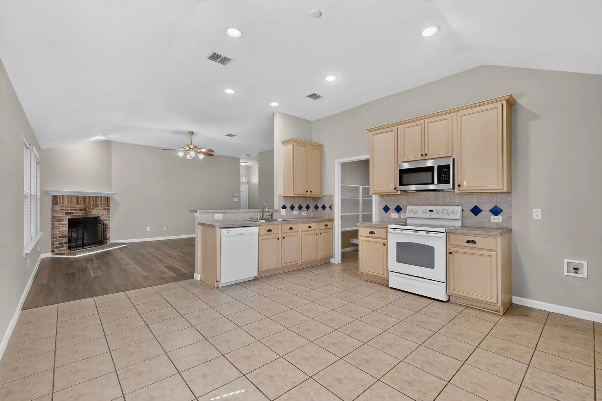 Open-concept kitchen featuring tile flooring, wood-finish cabinetry, a stainless steel microwave, and white appliances