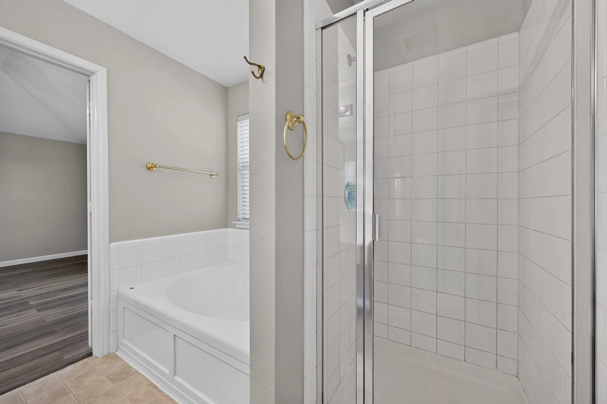 White tiled shower enclosure with clear glass door, alongside a built-in soaking tub with white tile surround