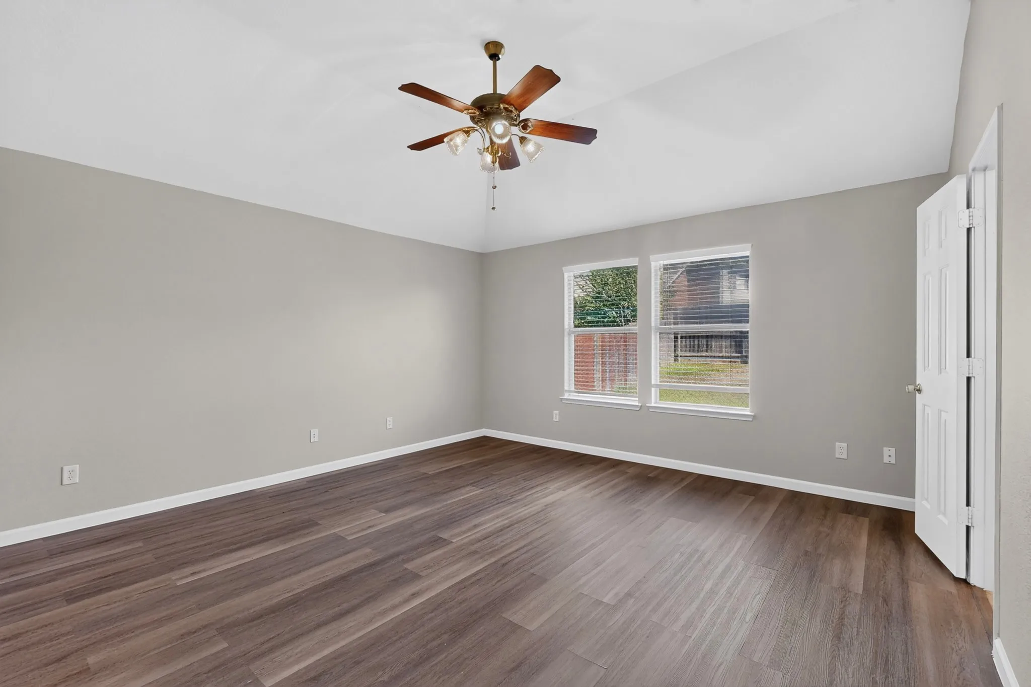 Spacious room featuring wood-finish flooring, two windows, and a ceiling fan with integrated lighting