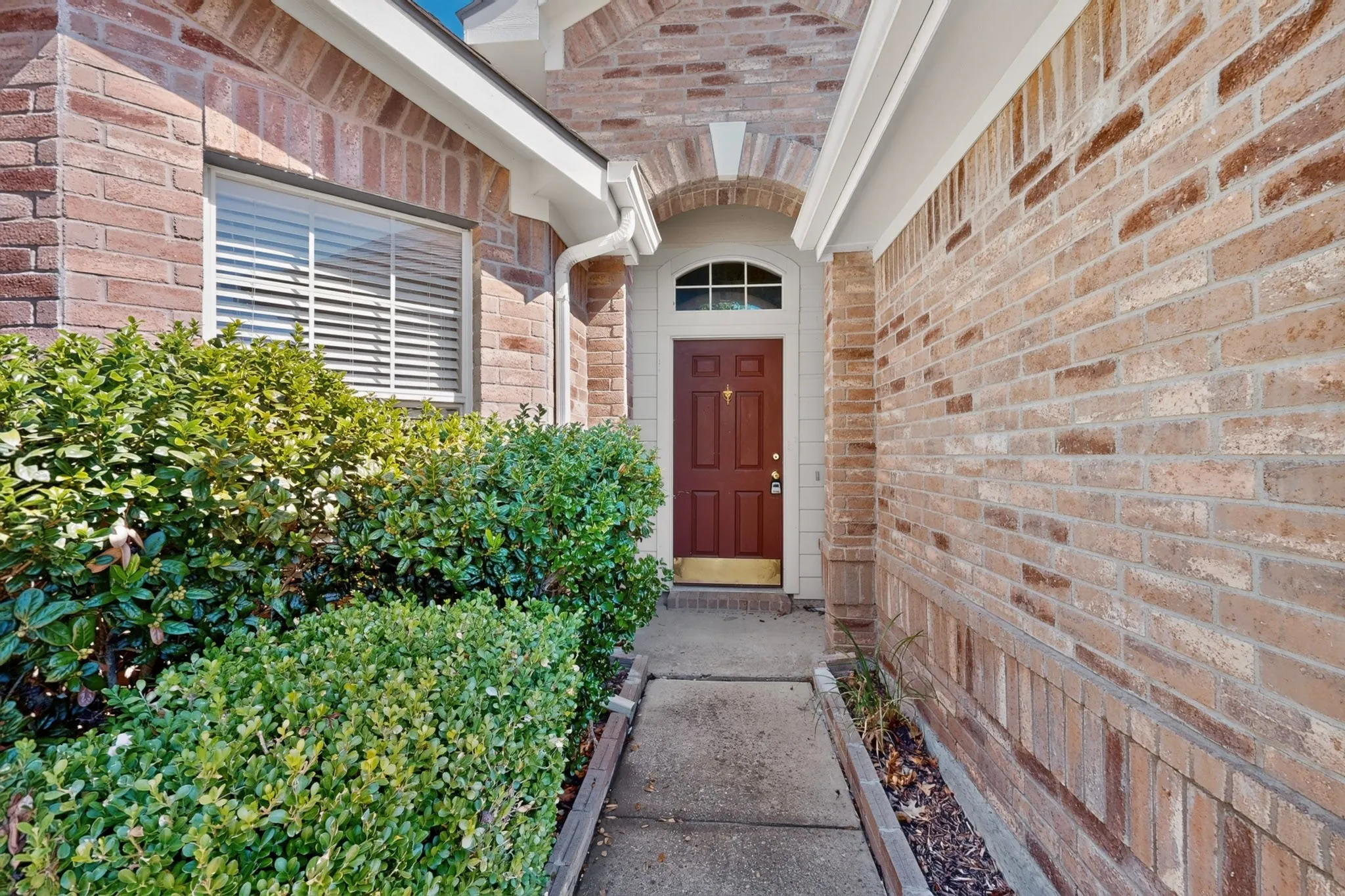 Brick exterior with an arched entryway, solid wood front door, and a transom window