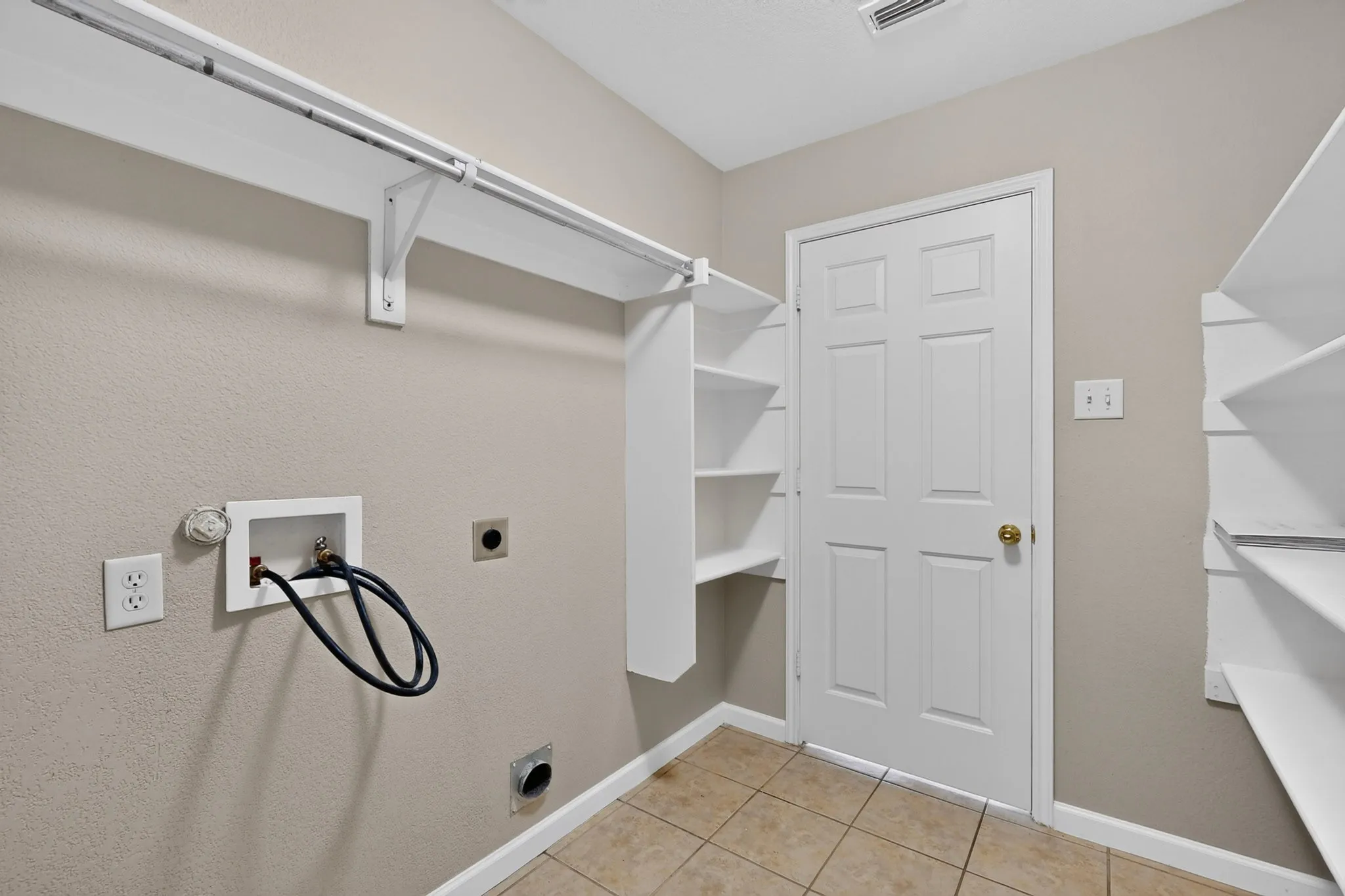 Dedicated laundry area featuring tile flooring, built-in shelving, and a hanging rod