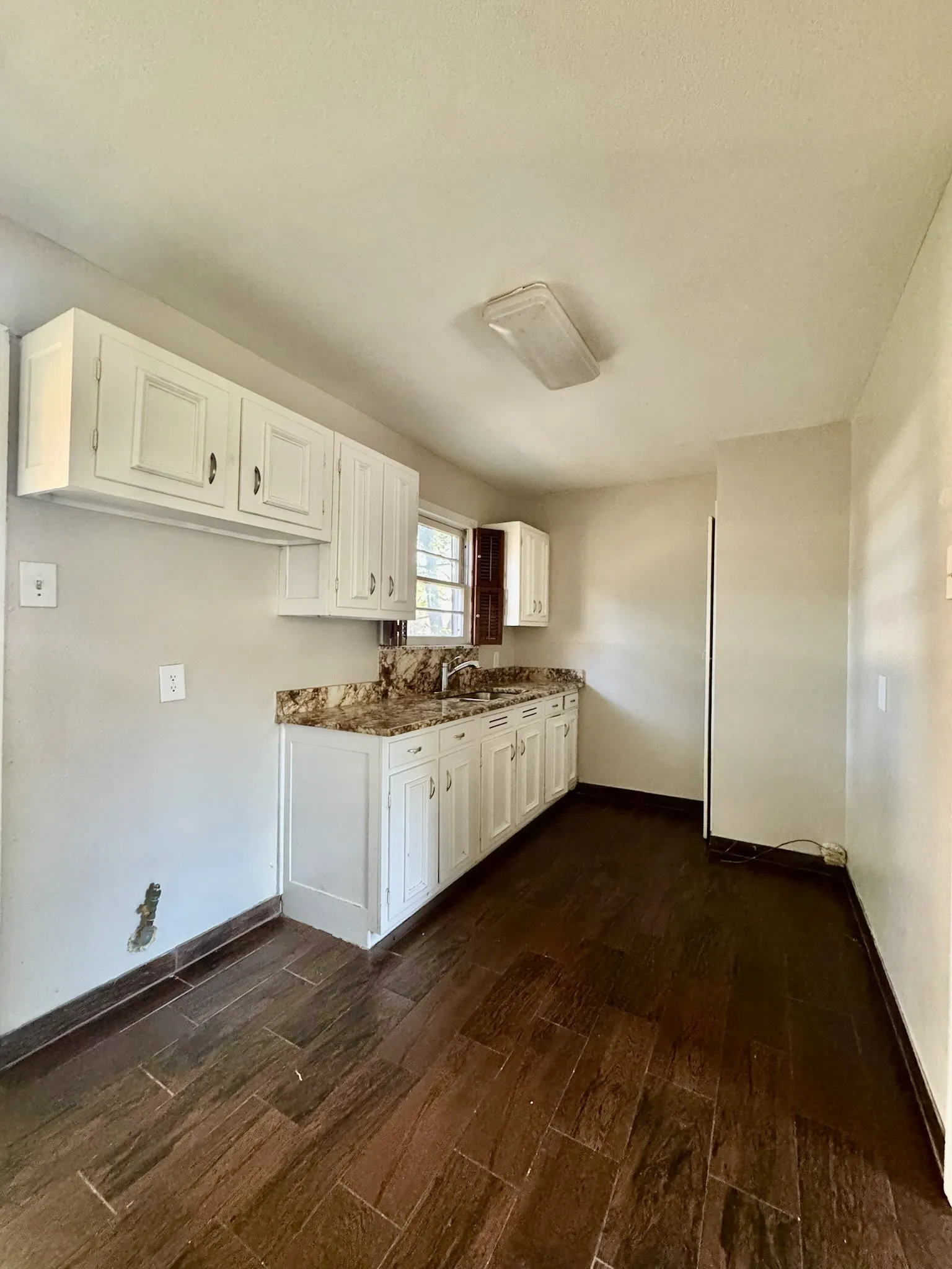 Wood-finish flooring throughout, white cabinetry, dark stone countertops, stainless steel sink, and ample storage