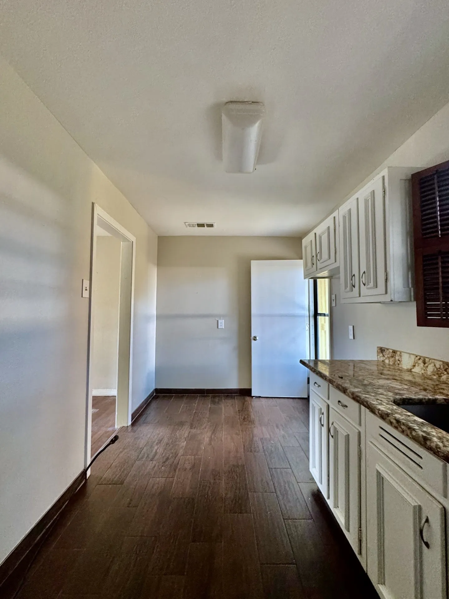 Galley kitchen with wood-finish flooring, white cabinetry, and granite countertops