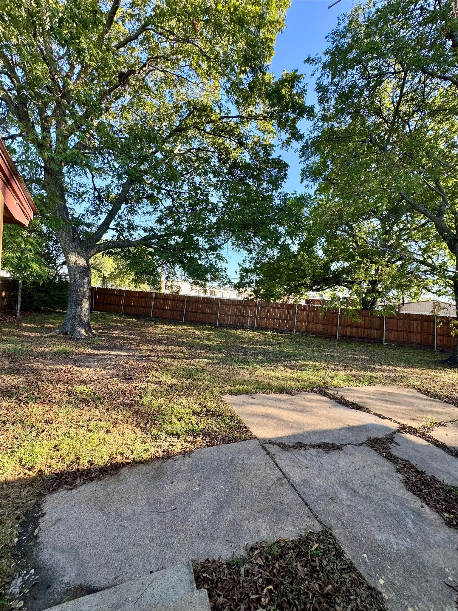 Expansive rear yard featuring a wood privacy fence, mature trees, and concrete patio