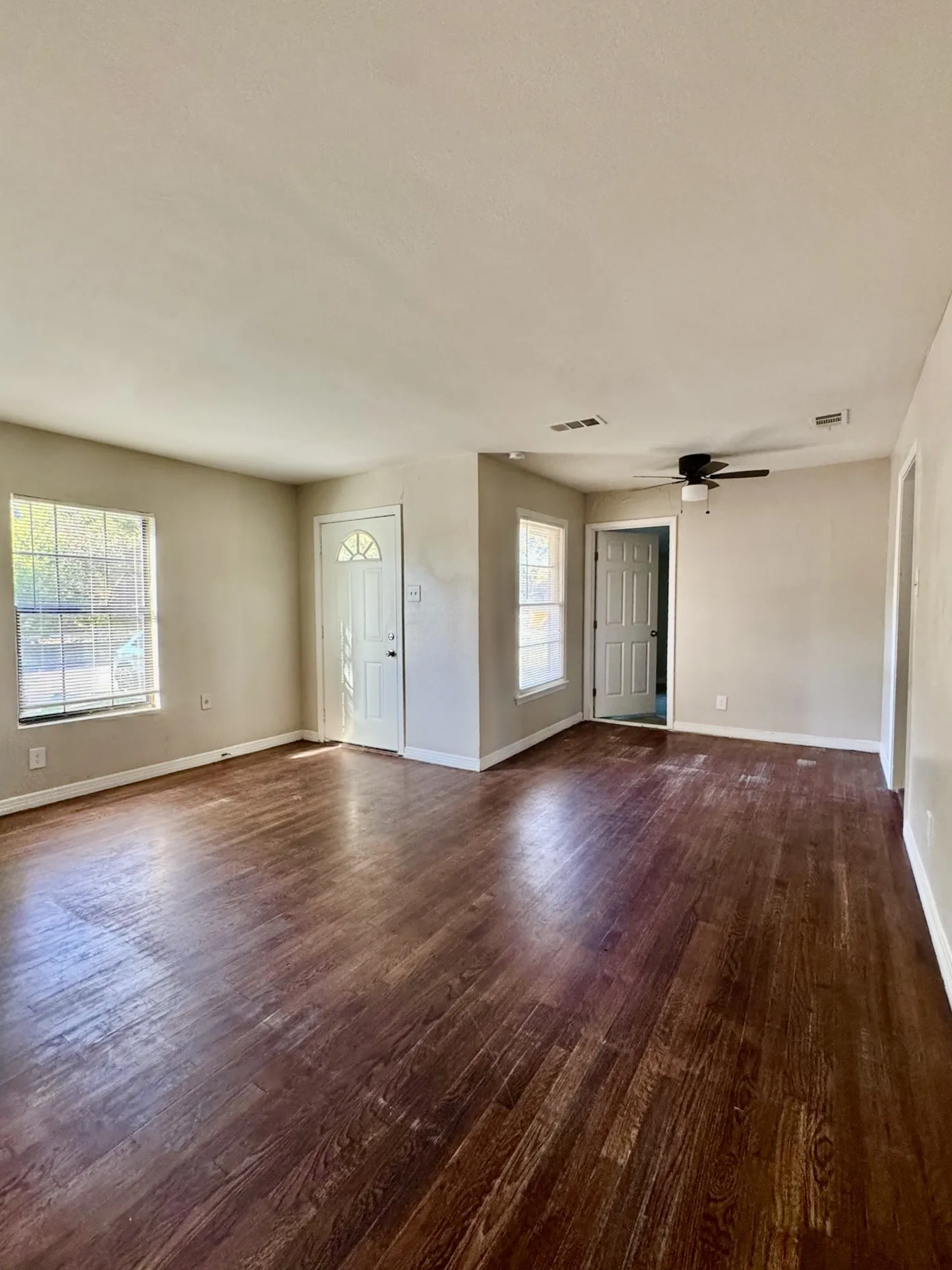 Spacious room featuring wood-finish flooring, multiple windows, a ceiling fan, and two panel doors